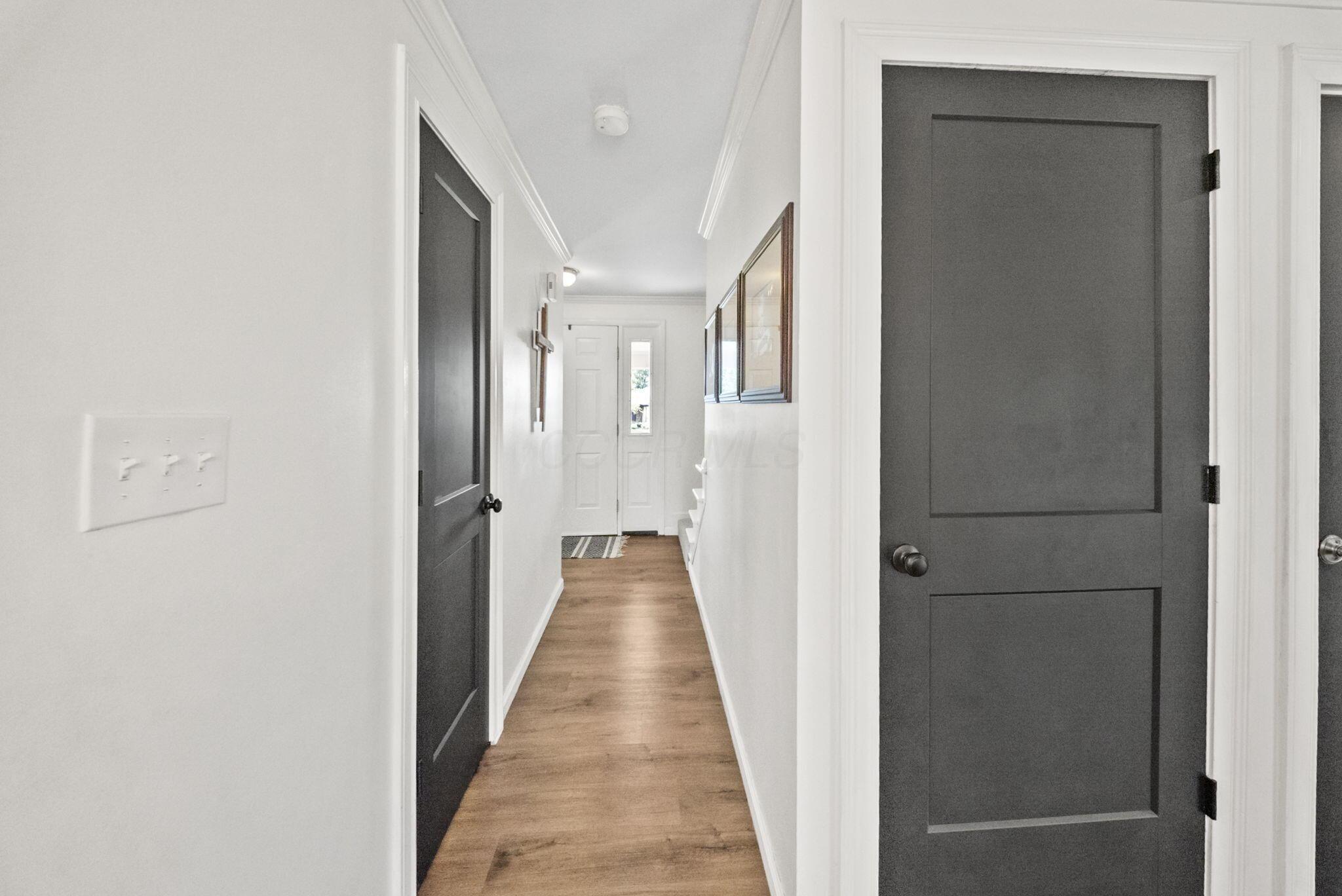 Bright hallway with wood floors, charcoal doors, framed art, and a front door with a narrow window.