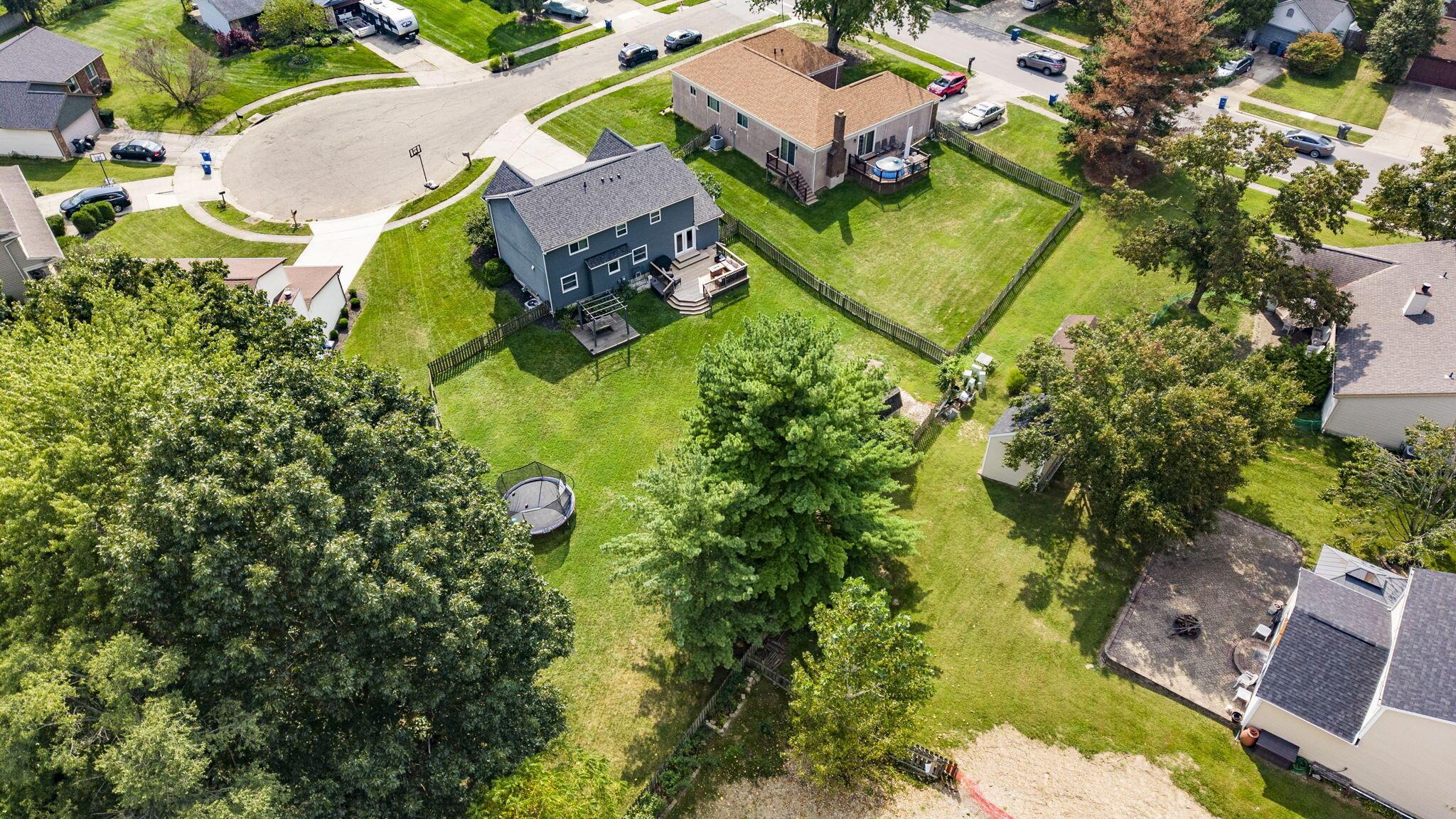 Aerial view of a home and its large fenced backyard with mature trees and a deck.