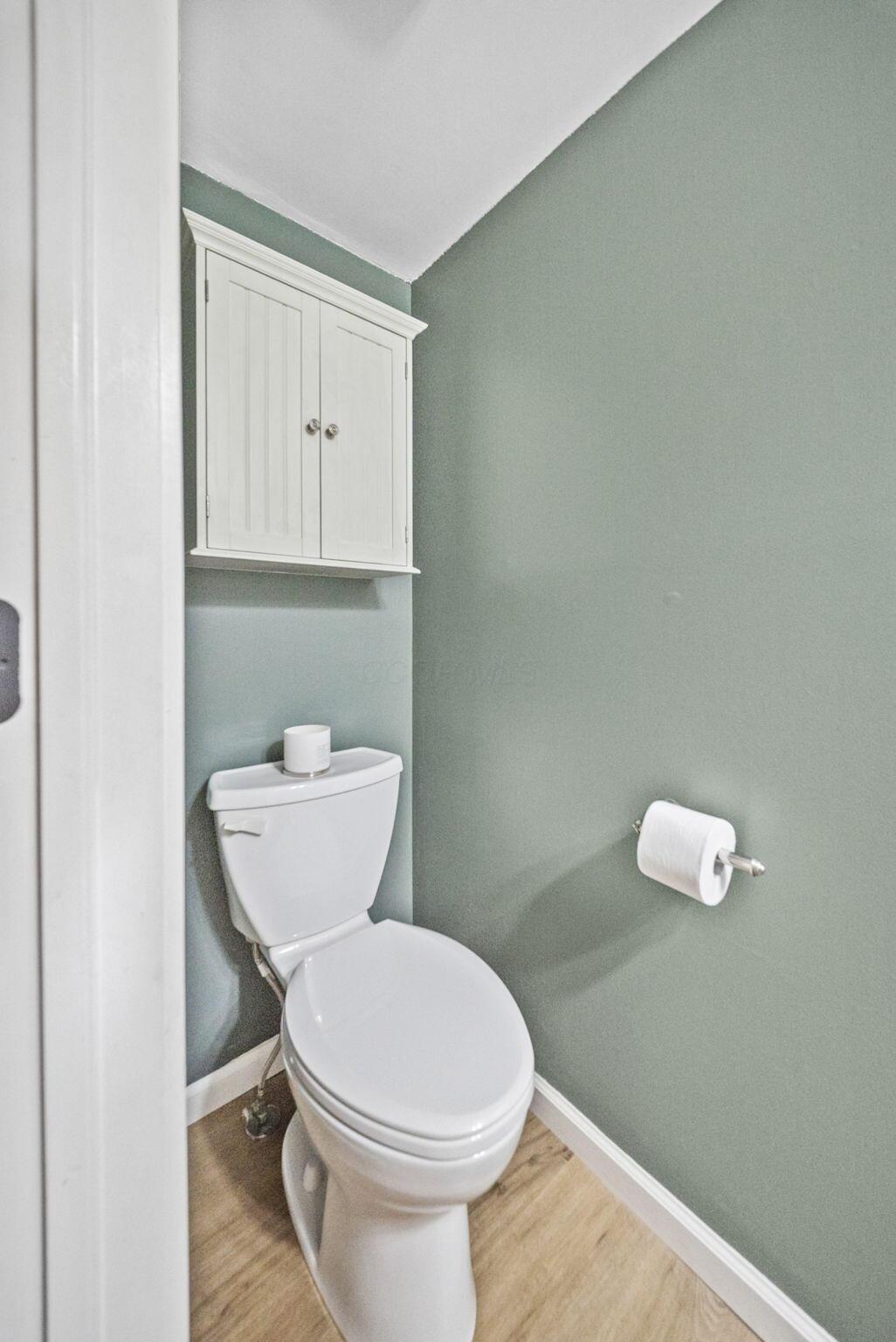 Compact bathroom with a white toilet, wall-mounted cabinet, and muted sage-green walls.
