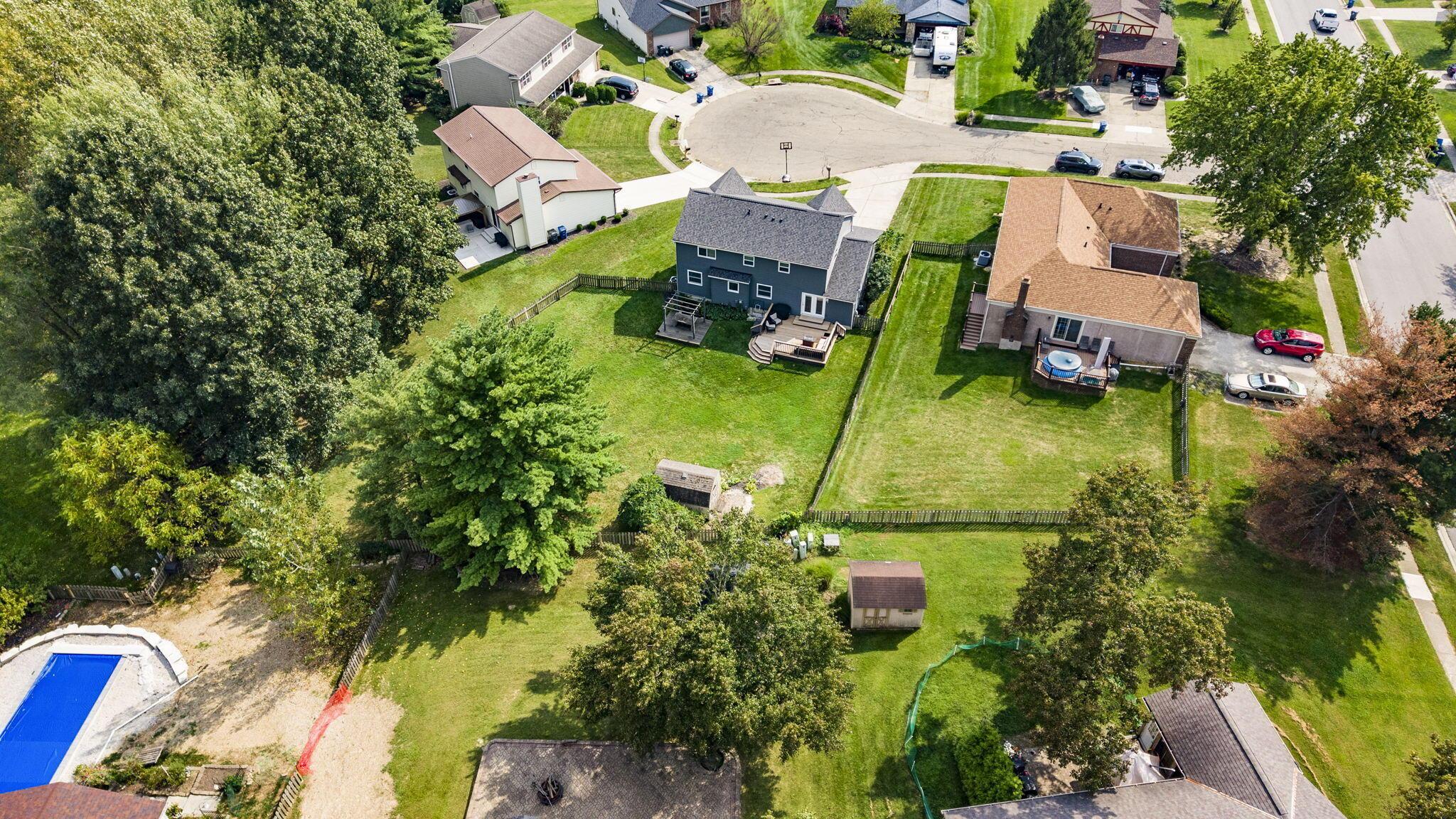 Aerial view of a blue two-story home with a rear deck and fenced lawn.