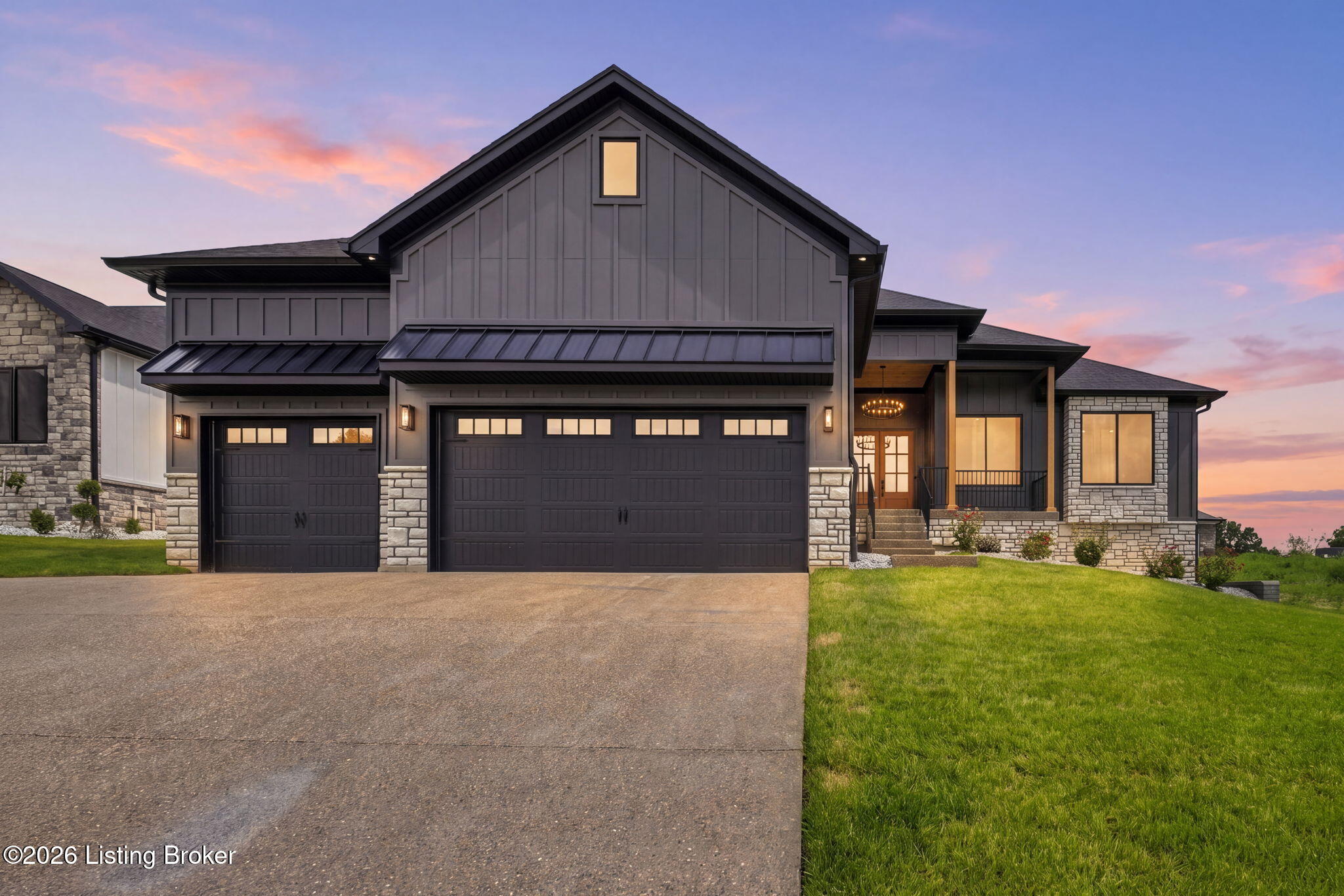 Modern gray home with stone accents, two garage doors, and a lit entrance at dusk.