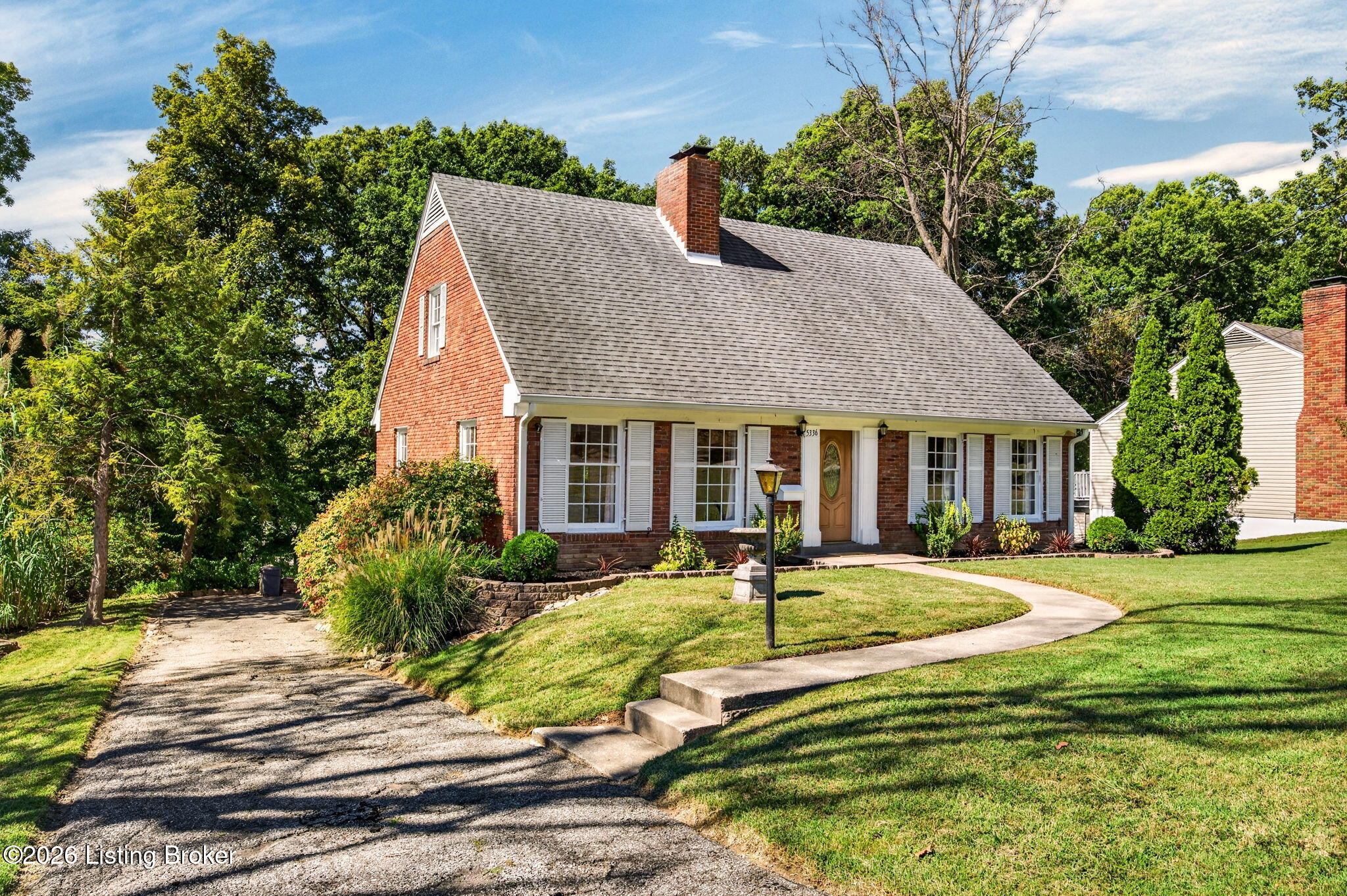 Red-brick house with white shutters, a steep gray roof, and a curved front walkway.