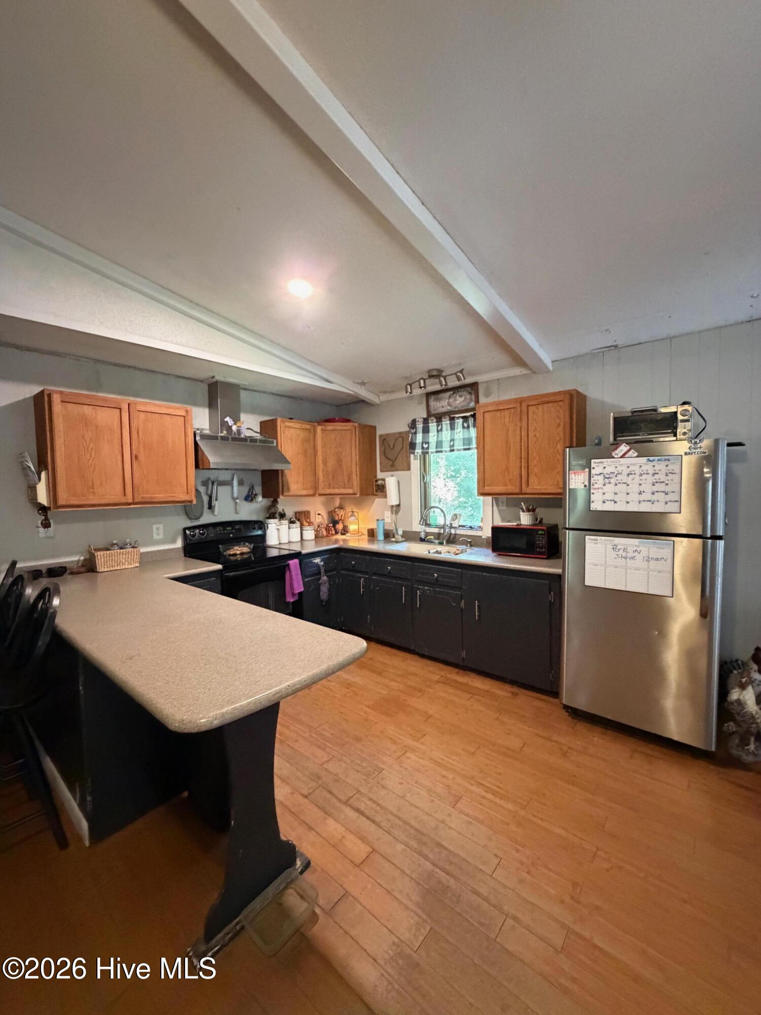 Kitchen with a large peninsula, two-tone cabinets, stainless steel refrigerator, and wood-look tile flooring.