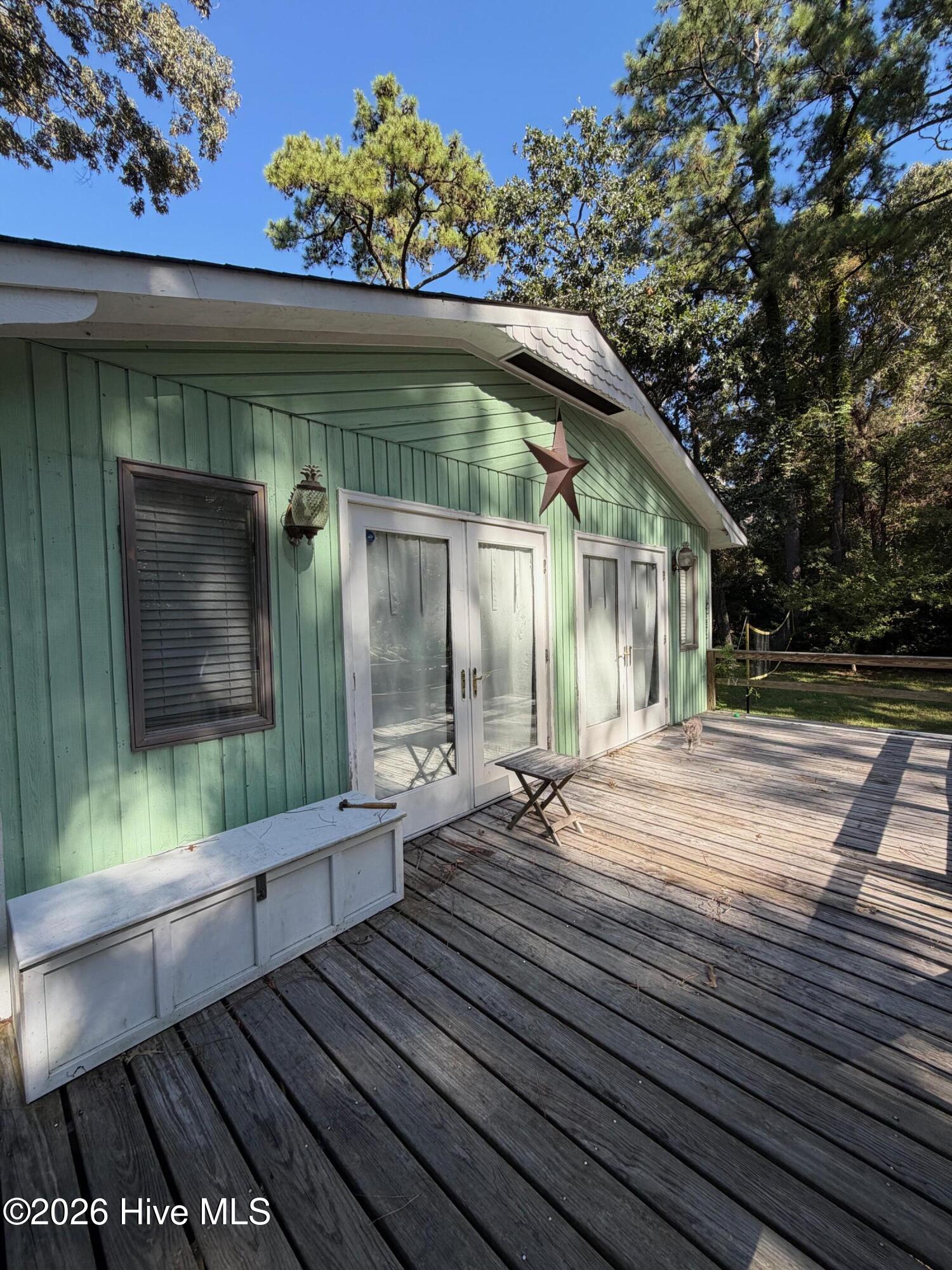 Wooden deck beside a mint-green house, with white French doors and a metal star on the siding.