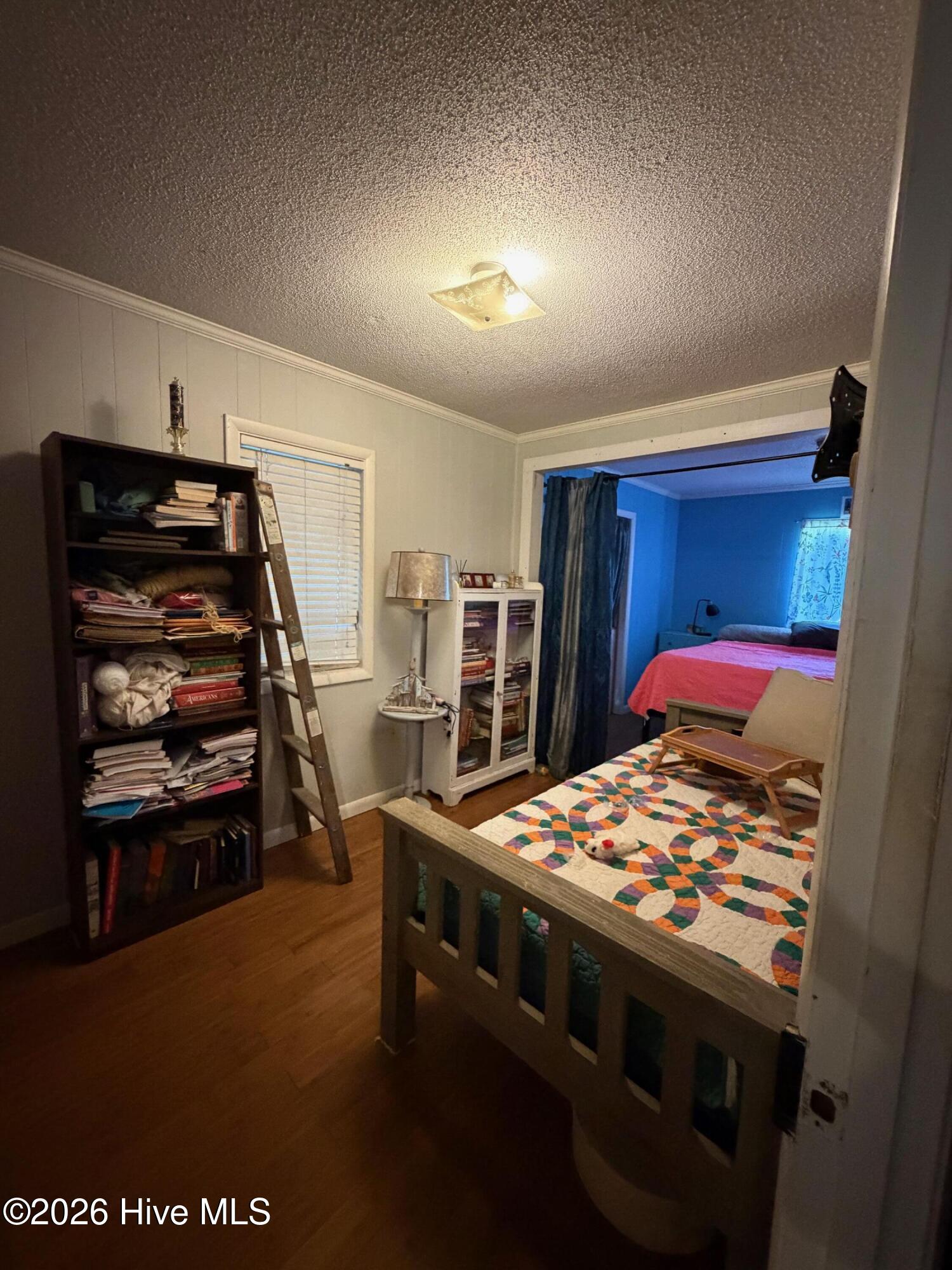 Bedroom with a colorful geometric quilt, crowded bookcase, and adjoining bedroom visible through a wide opening.