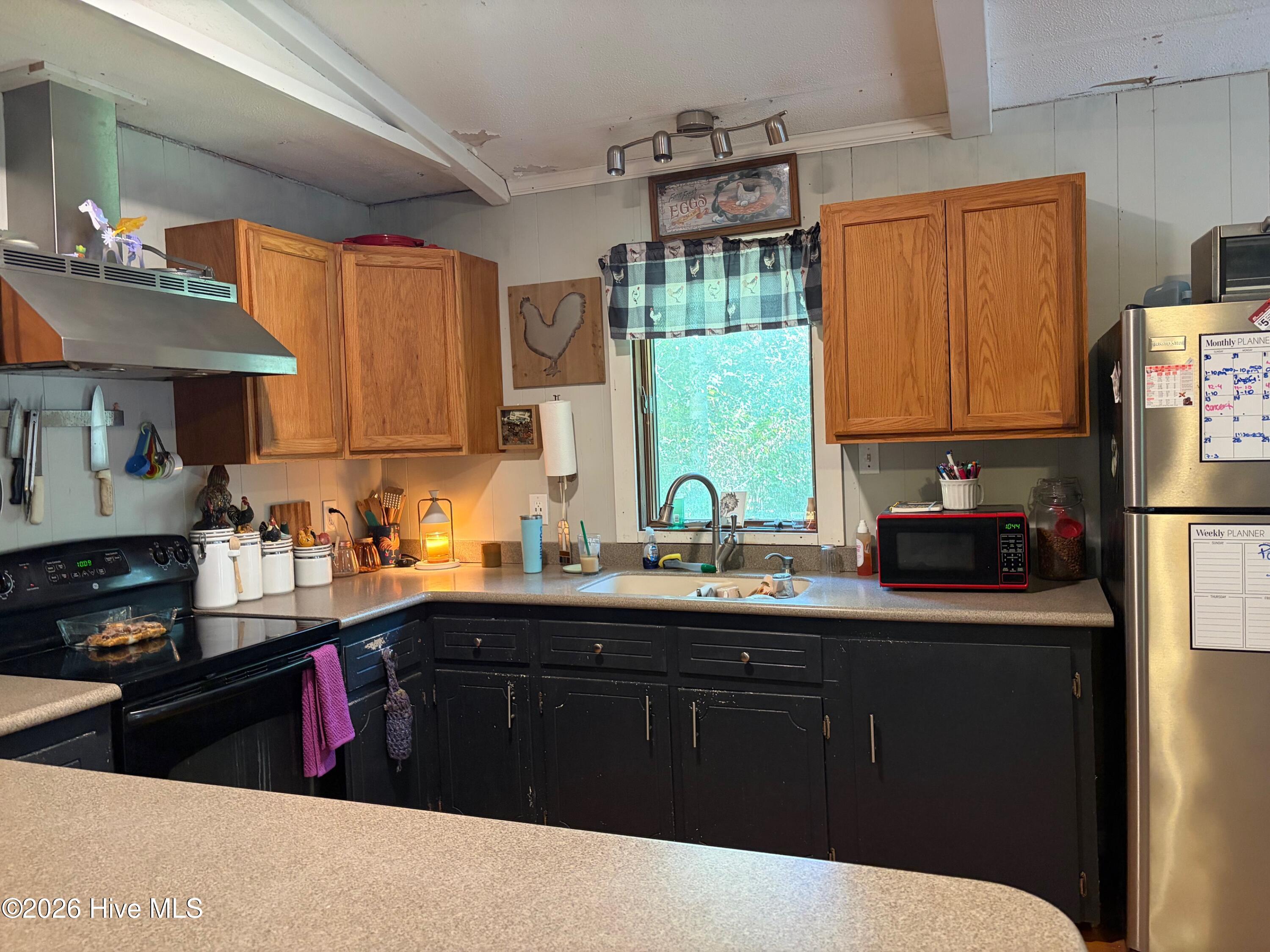 Kitchen with dark lower cabinets, oak upper cabinets, and a sink beneath a window.