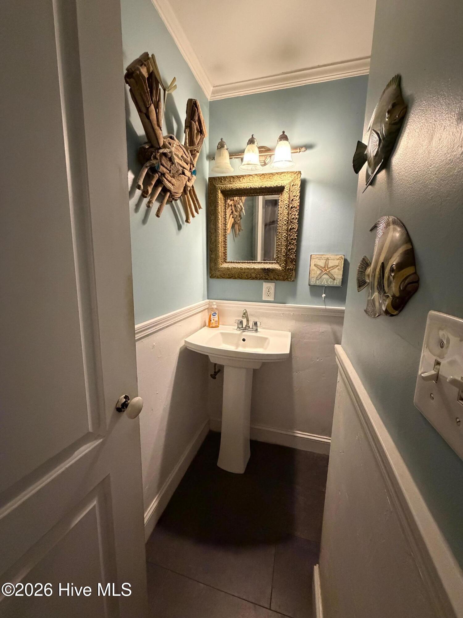 Bathroom with a pedestal sink, ornate gold-framed mirror, blue walls, and fish decorations.