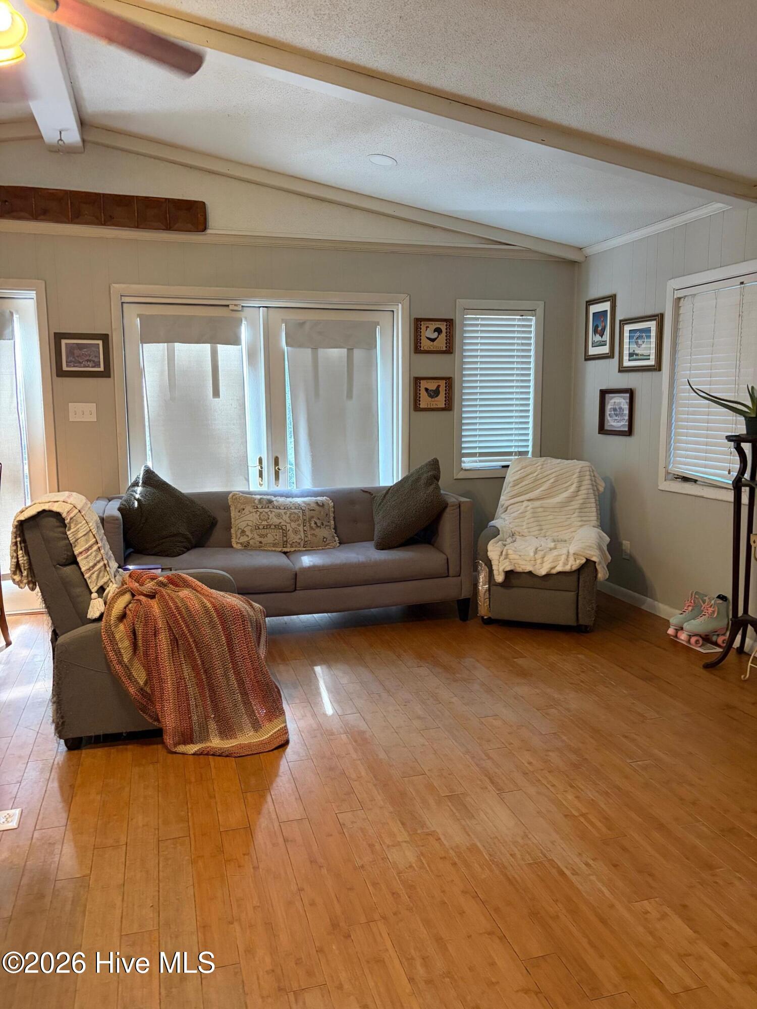Living room with vaulted ceiling, wood floors, gray seating, and colorful knitted throws.