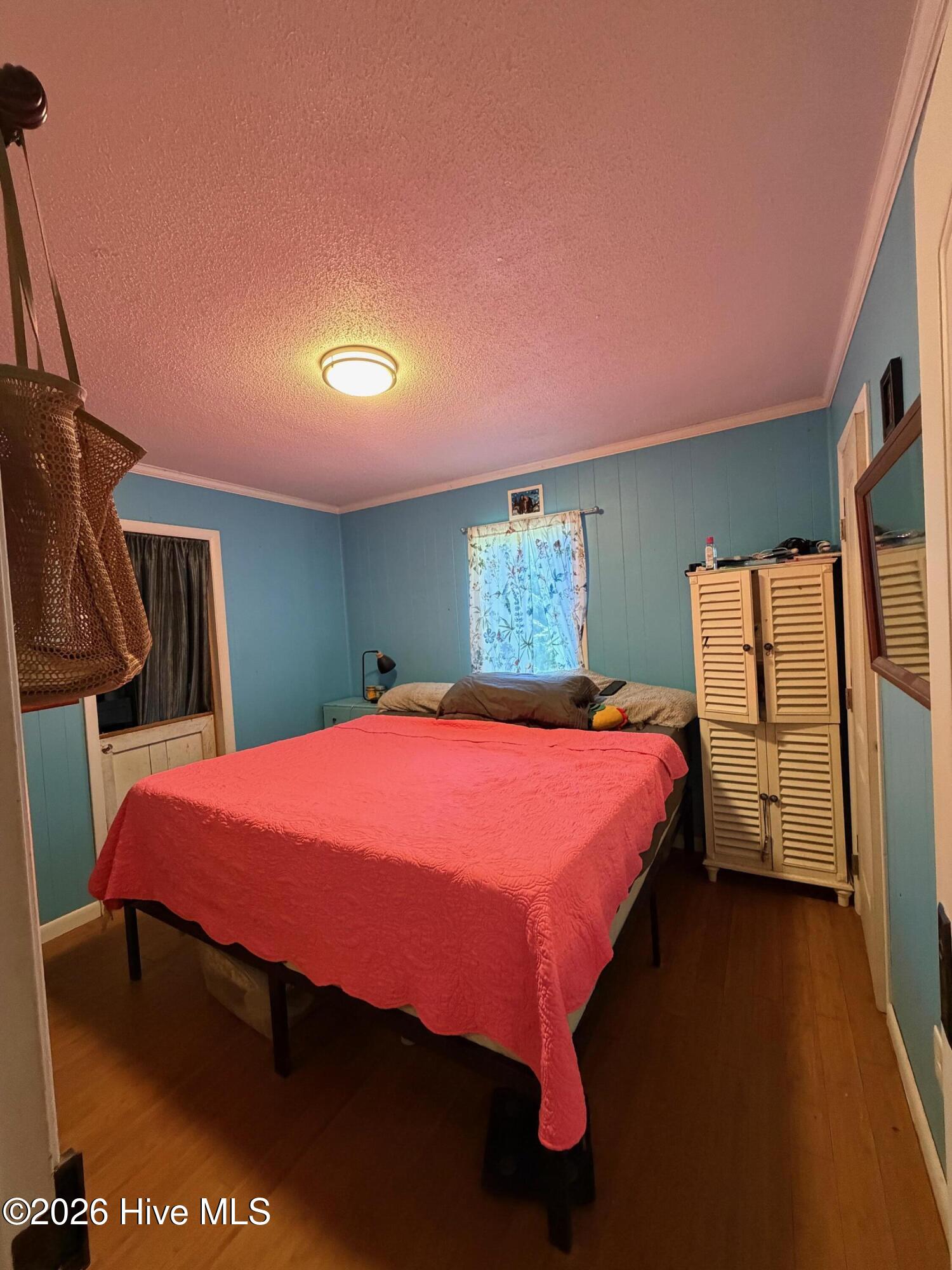 Bedroom with teal walls, a coral quilt, floral window curtains, and a louvered wardrobe.