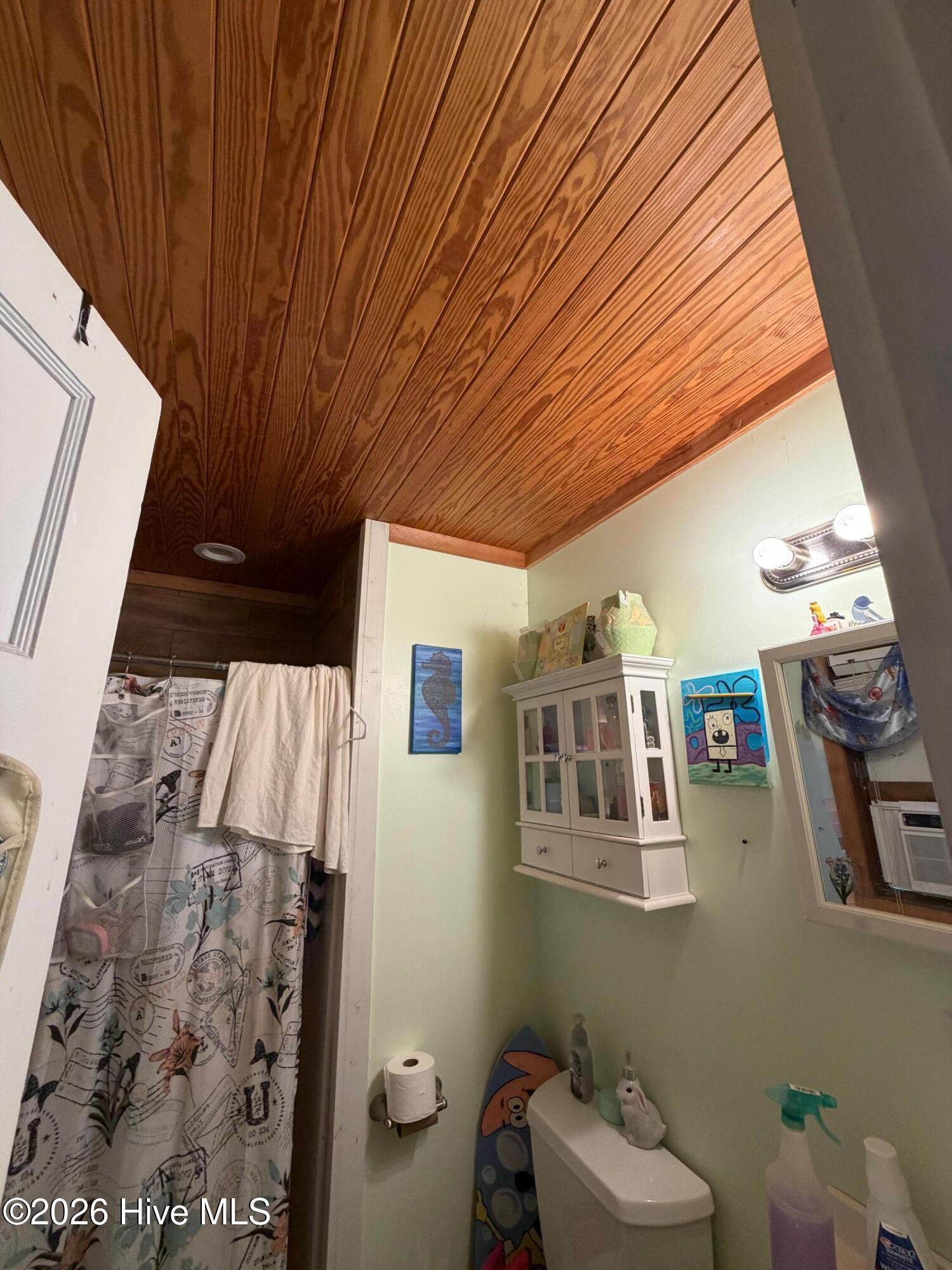 Bathroom with a warm wood-plank ceiling and patterned shower curtain.