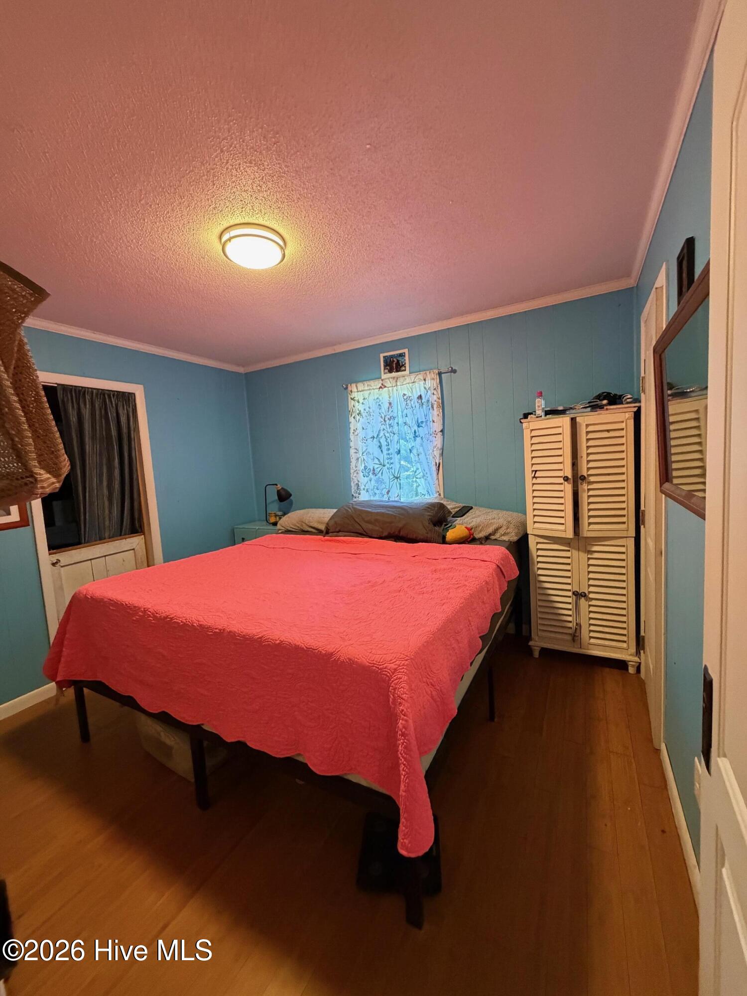 Bedroom with blue walls, wood floors, a coral quilt, and a louvered wardrobe.
