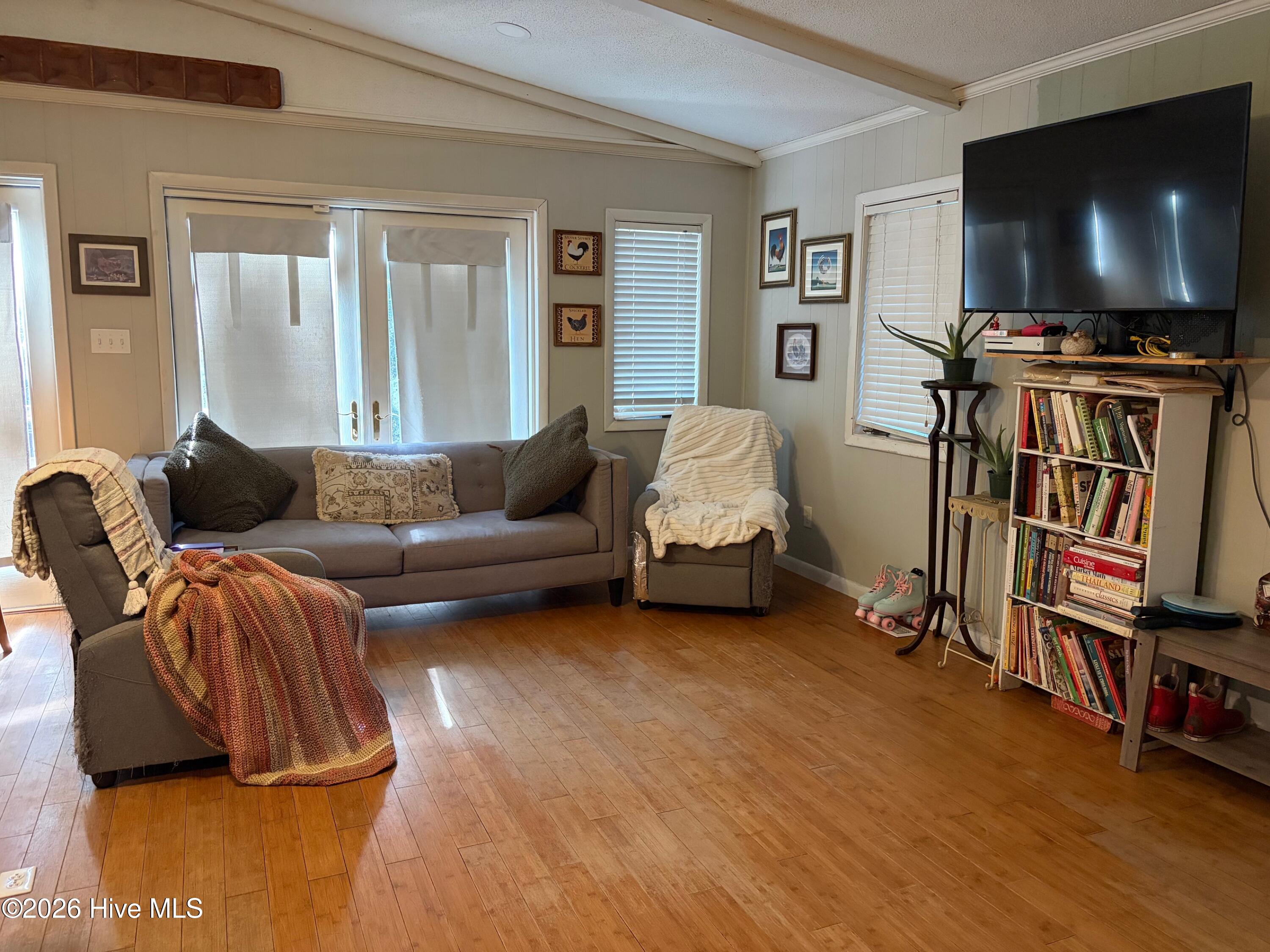 Living room with gray seating, warm wood floors, sliding glass doors, and a wall-mounted television.