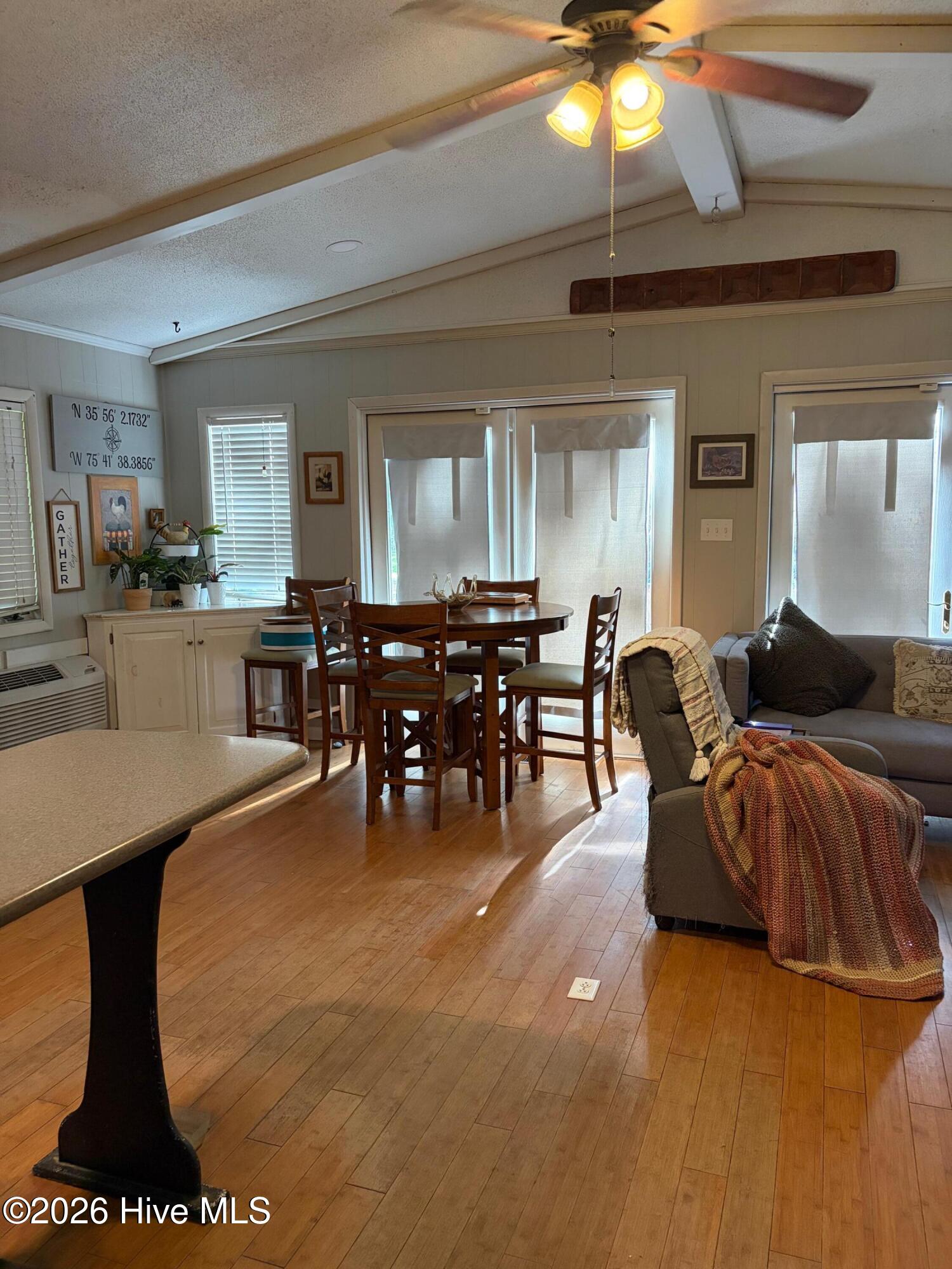 Open living and dining area with vaulted ceiling, hardwood floors, a round table, and gray seating.
