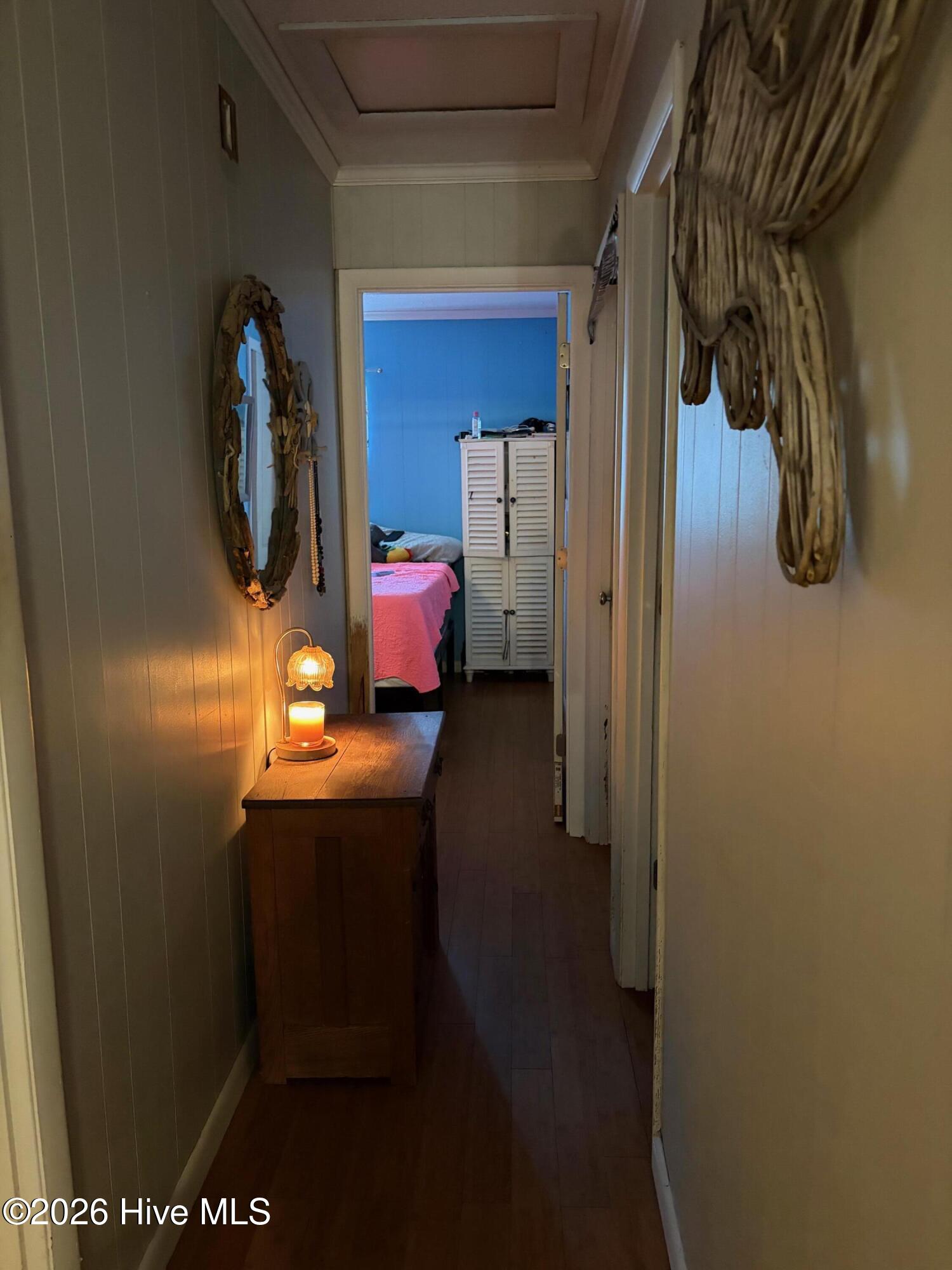 Furnished hallway leading to a blue bedroom, with a lit lamp and candle on a wooden table.