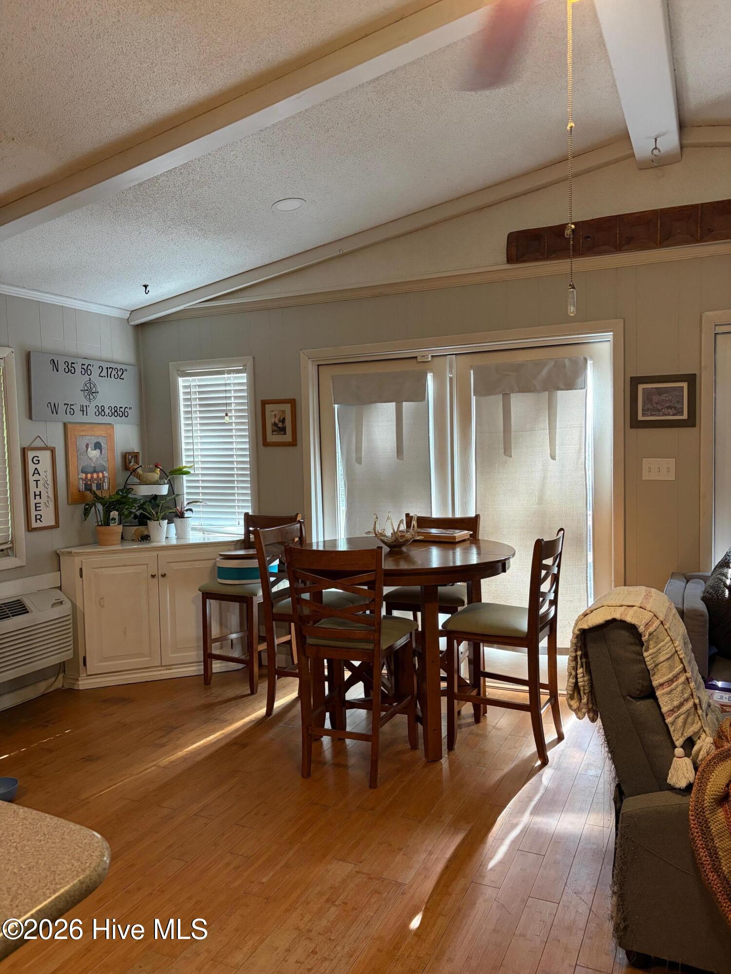 Dining area with round wooden table, vaulted ceiling, and sliding glass doors.