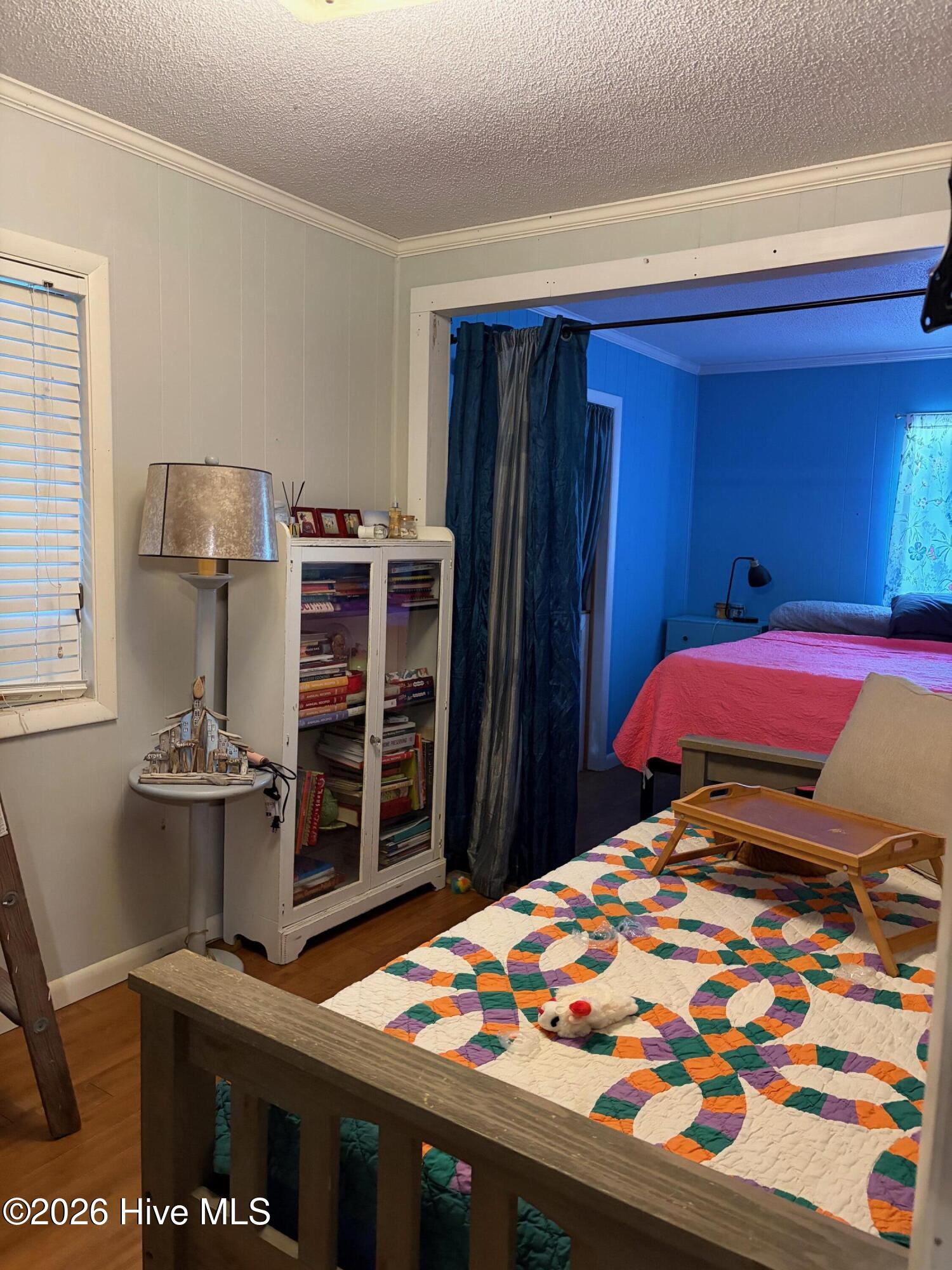 Bedroom with colorful patchwork quilt, glass-front bookcase, and adjoining blue bedroom.