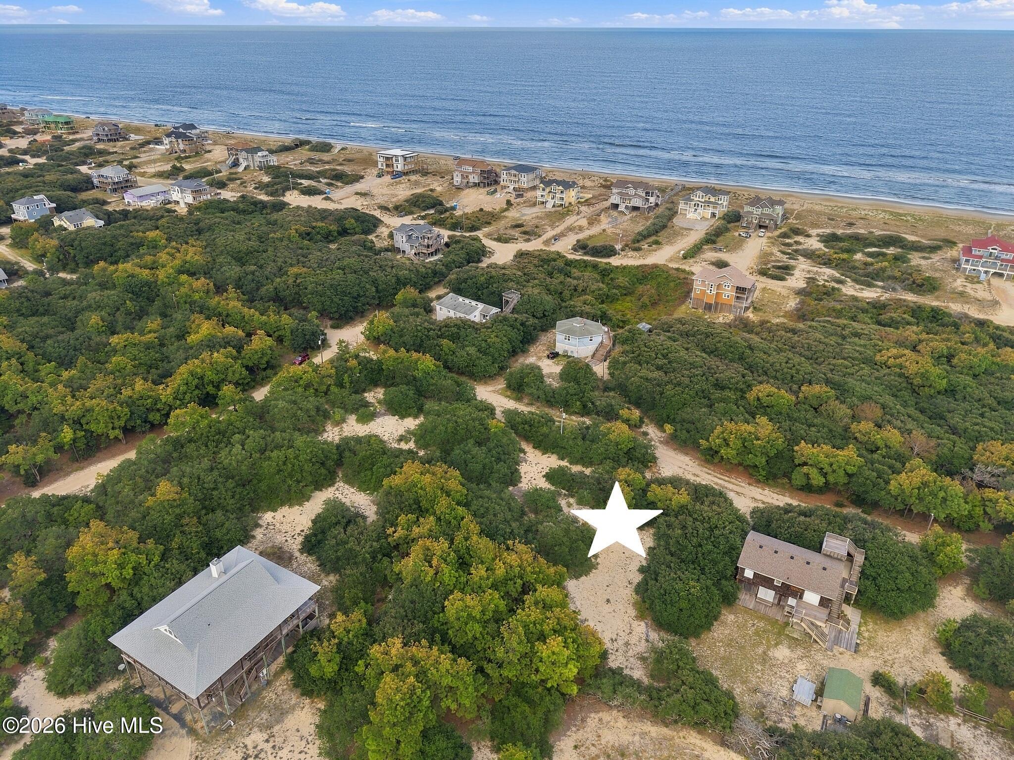 Aerial view of a star-marked lot amid coastal vegetation, homes, and the ocean.