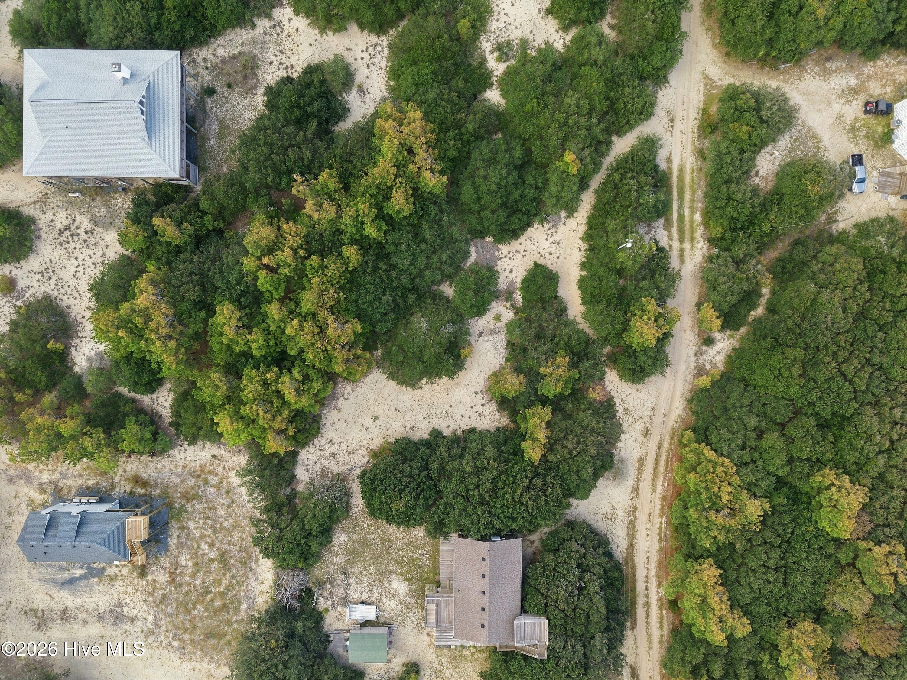 Aerial view of a sandy, tree-covered property beside a dirt road and nearby homes.