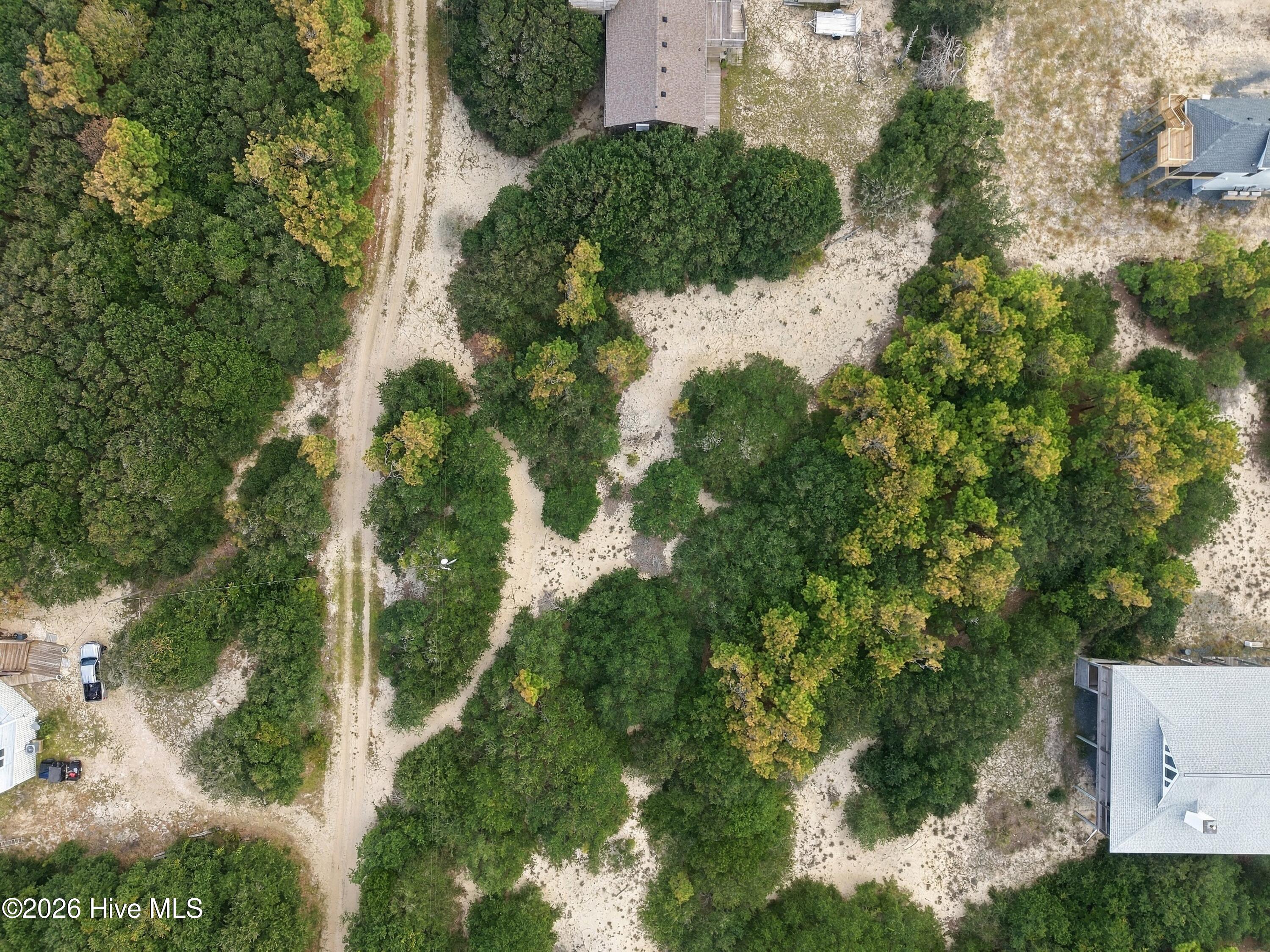 Aerial view of a wooded sandy lot with neighboring homes and sandy roads.