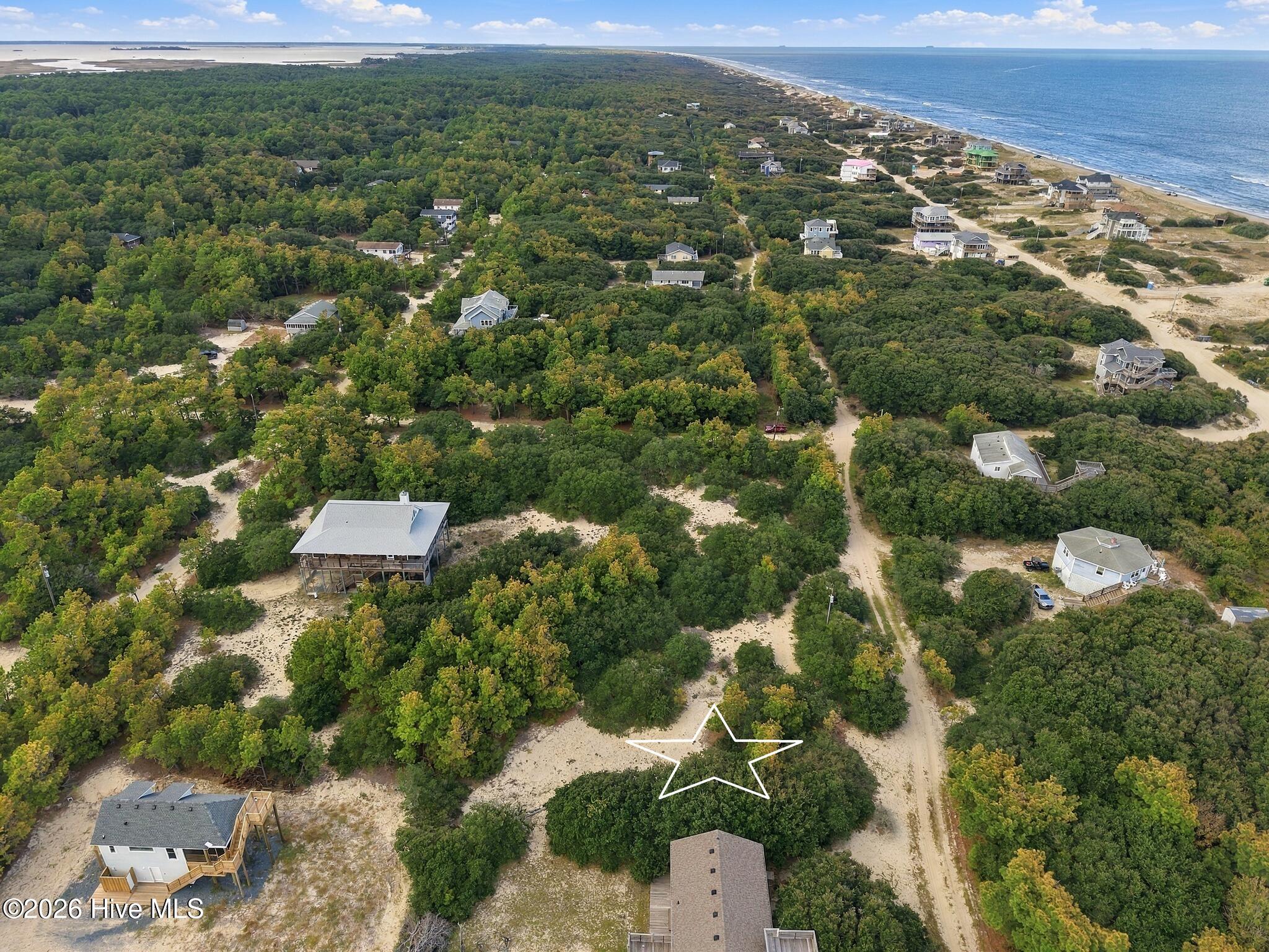Aerial view of a wooded coastal lot outlined by a white star, with homes and ocean shoreline nearby.