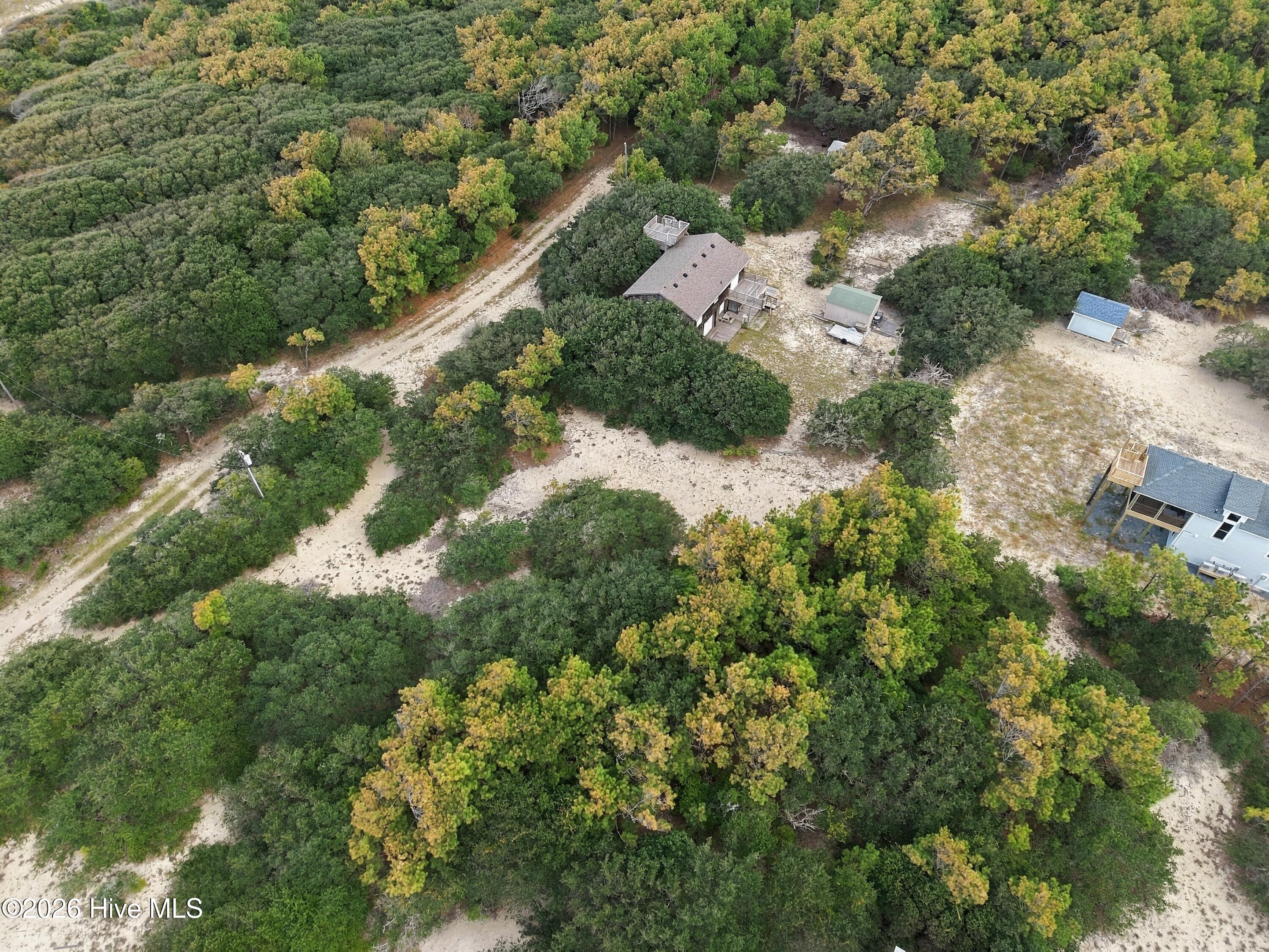 Aerial view of a house with elevated decks in a sandy clearing surrounded by dense trees.