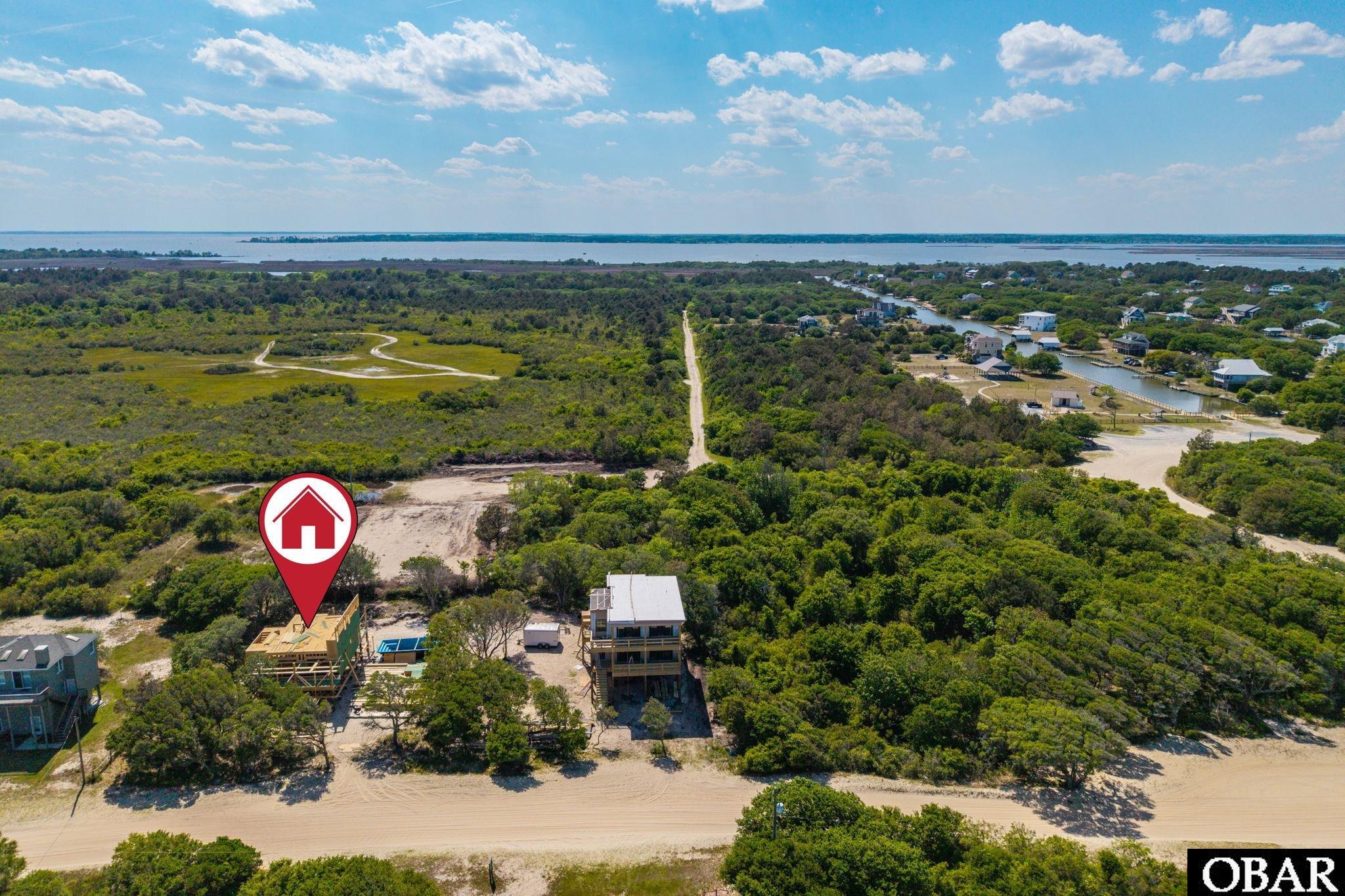 Aerial view of a house under construction beside coastal vegetation, with canals and water in the distance.