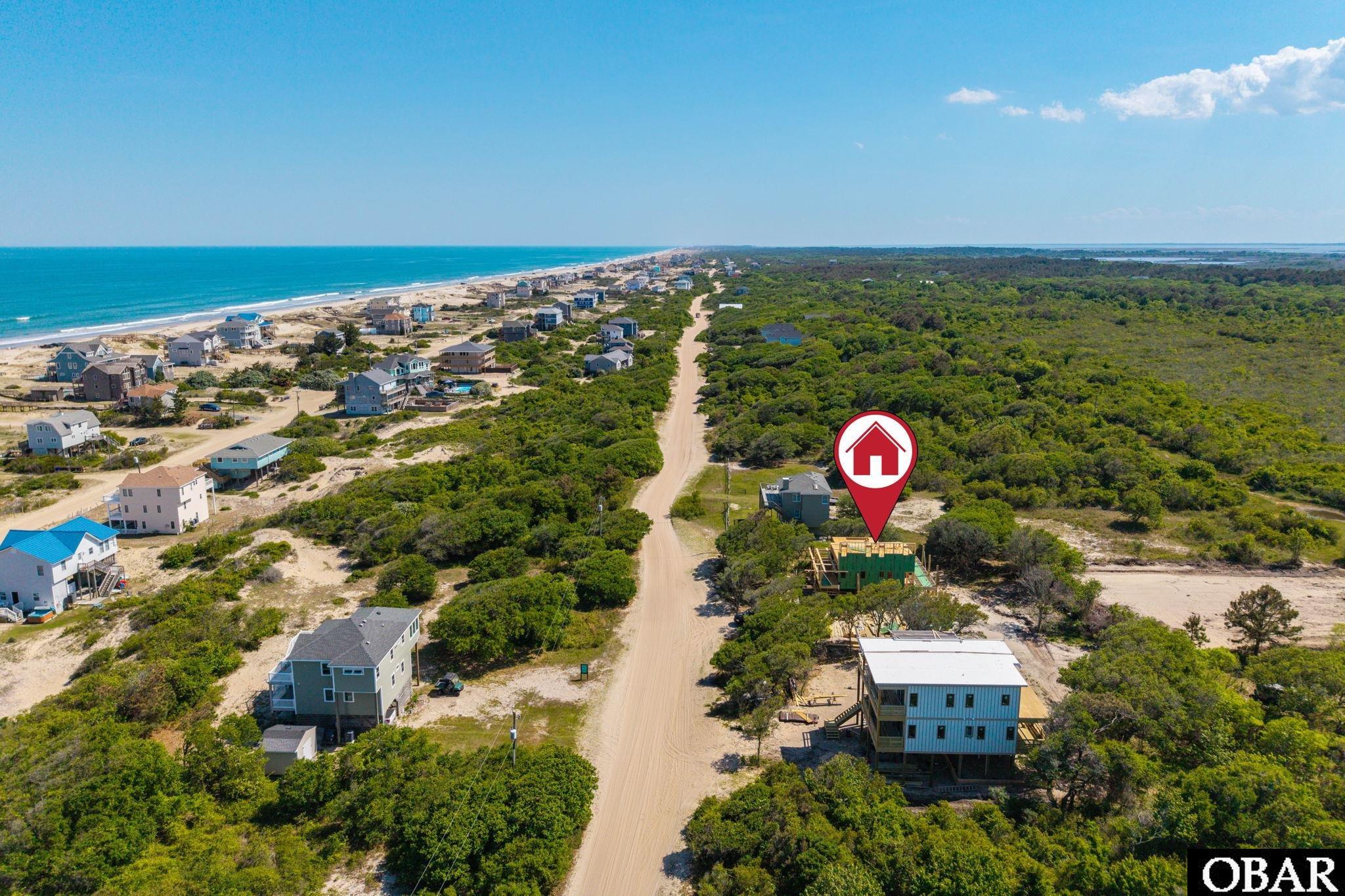 Coastal neighborhood beside the ocean, with a red pin marking a building under construction along a sandy road.