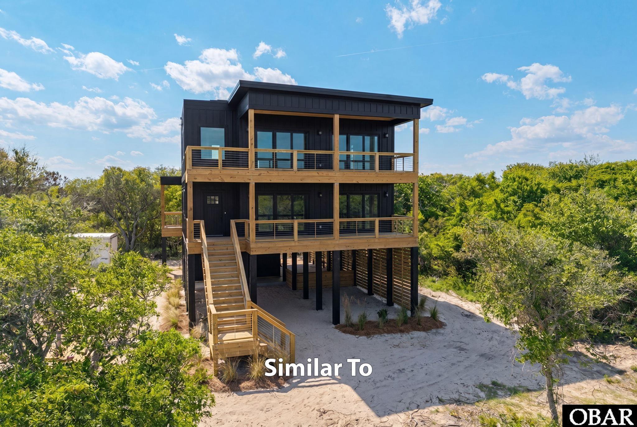 Elevated dark-sided coastal home with broad wood balconies and exterior stairs amid sandy, wooded surroundings.
