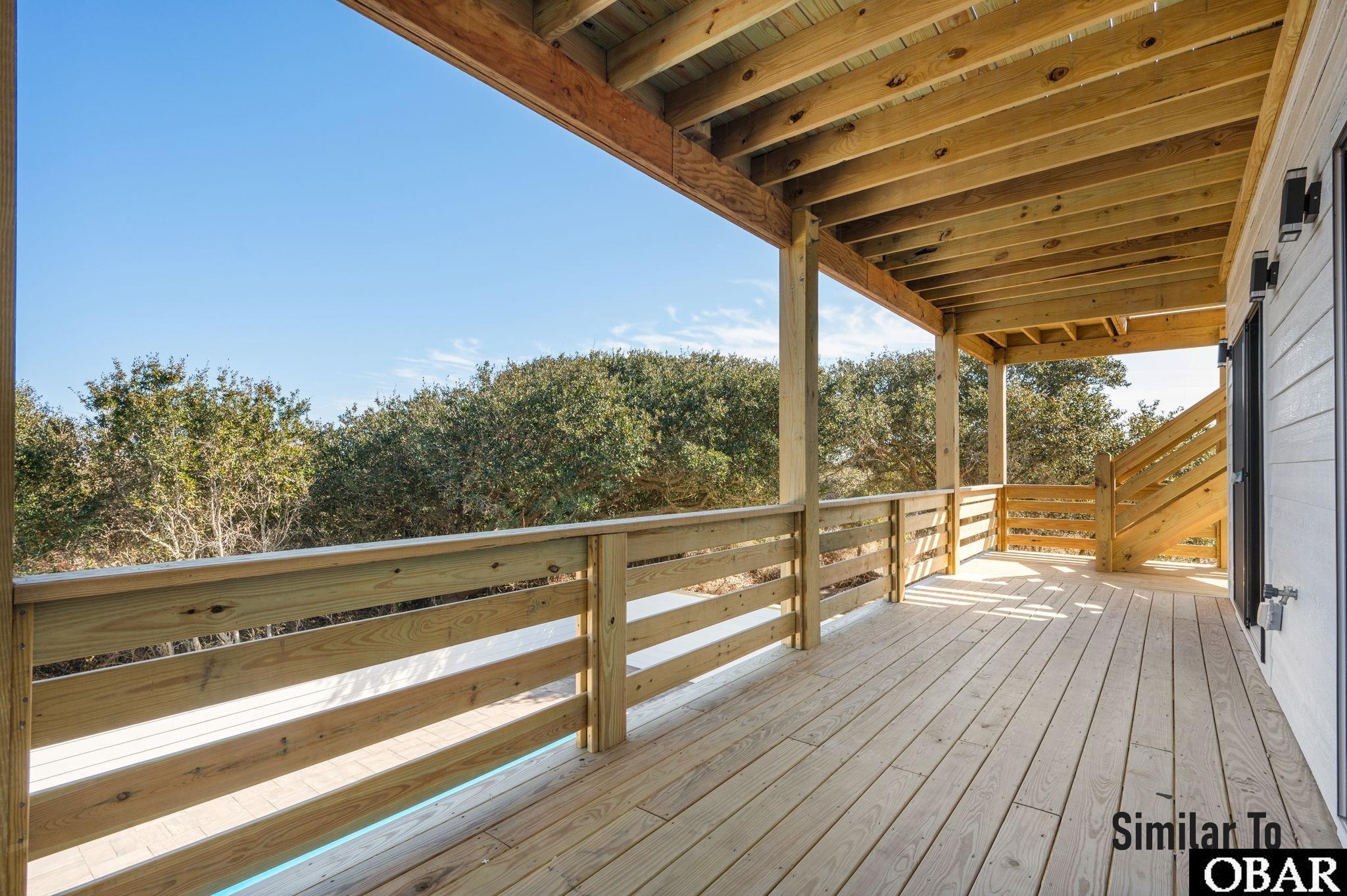 Covered wooden deck with exposed beams, timber railings, and trees beyond.