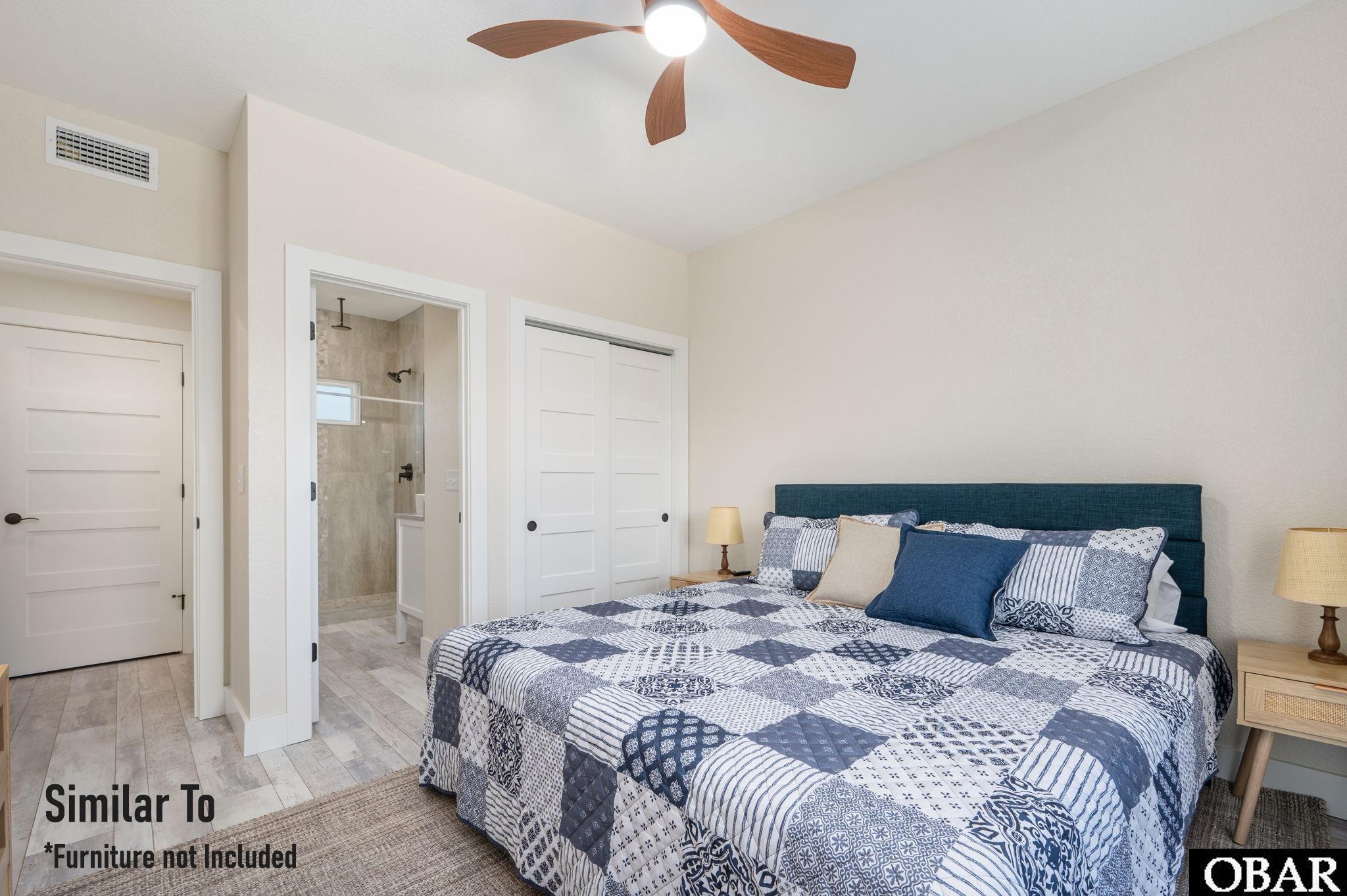 Bedroom with blue headboard and patterned quilt, with an ensuite bathroom visible through the doorway.