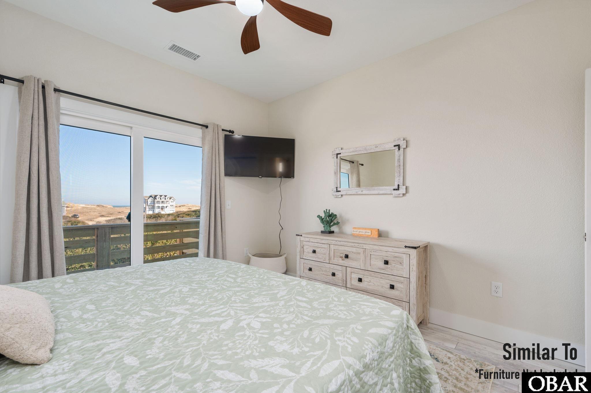 Bedroom with a patterned bedspread and sliding doors overlooking the ocean and a neighboring house.