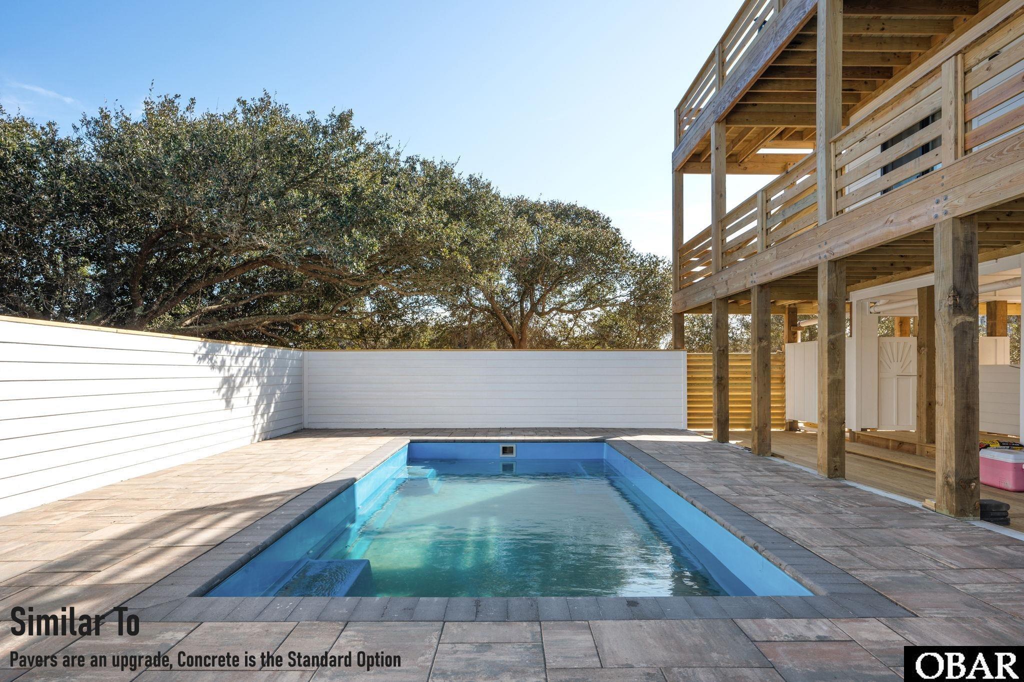 Rectangular backyard pool beside a raised wooden deck, enclosed by a white privacy fence and mature trees.