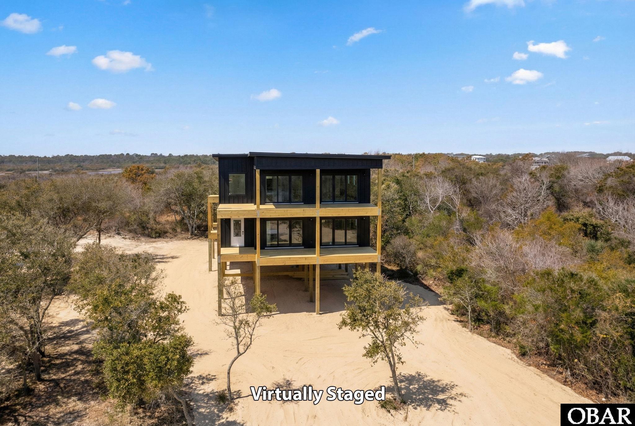 Modern raised two-story home with wood balconies on a sandy, tree-lined lot.