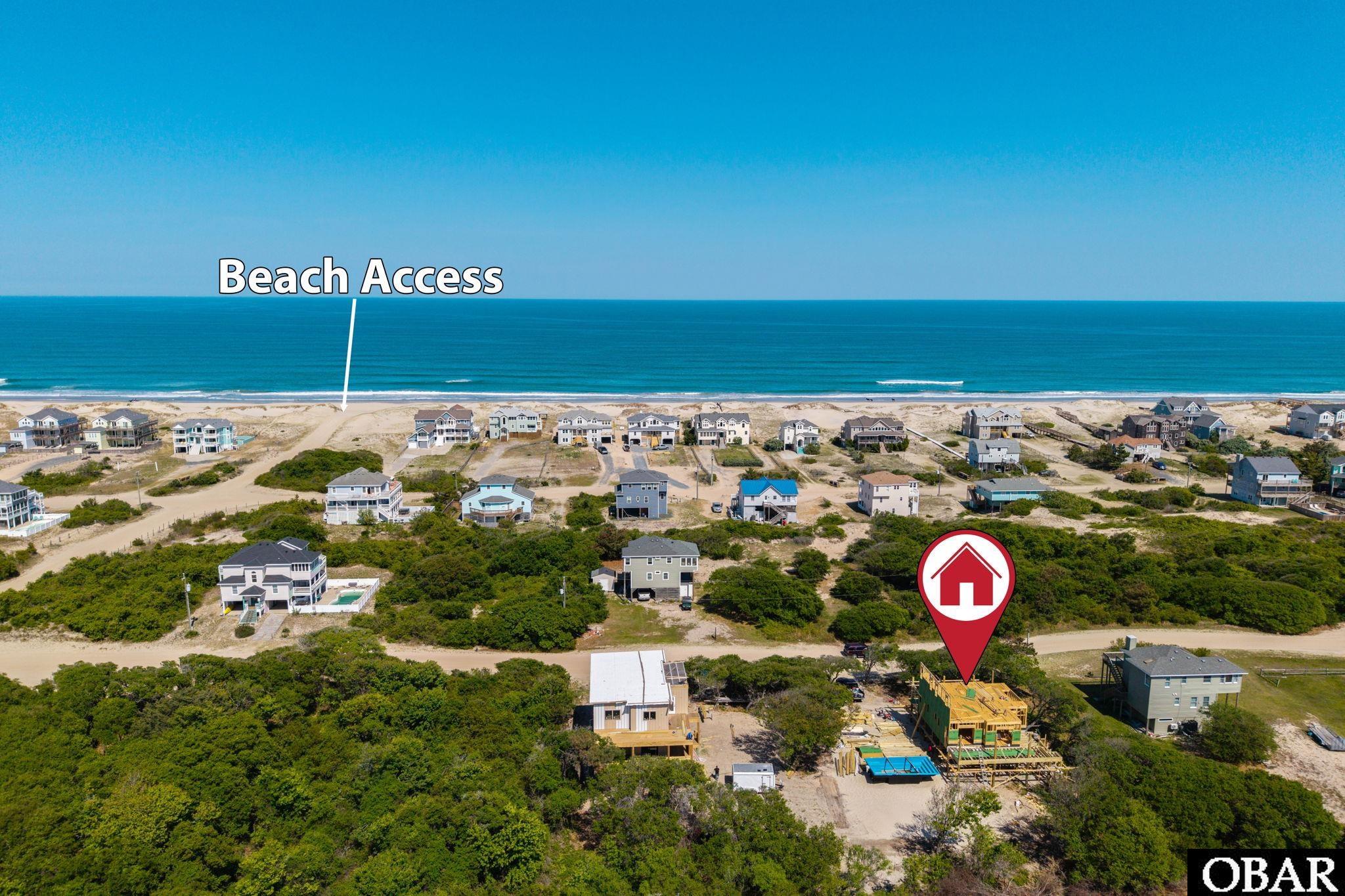 Aerial view of a home under construction near beach access, with the ocean beyond the coastal neighborhood.