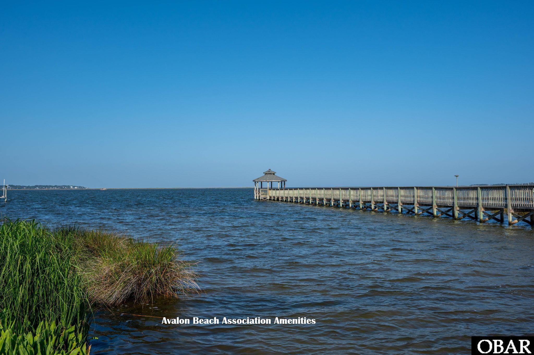 Wooden pier with a covered gazebo extends over the water beside shoreline grasses.