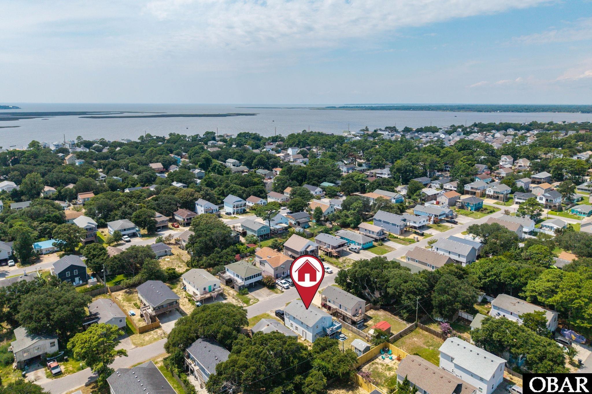 Aerial view of the marked property among coastal homes, with water beyond.