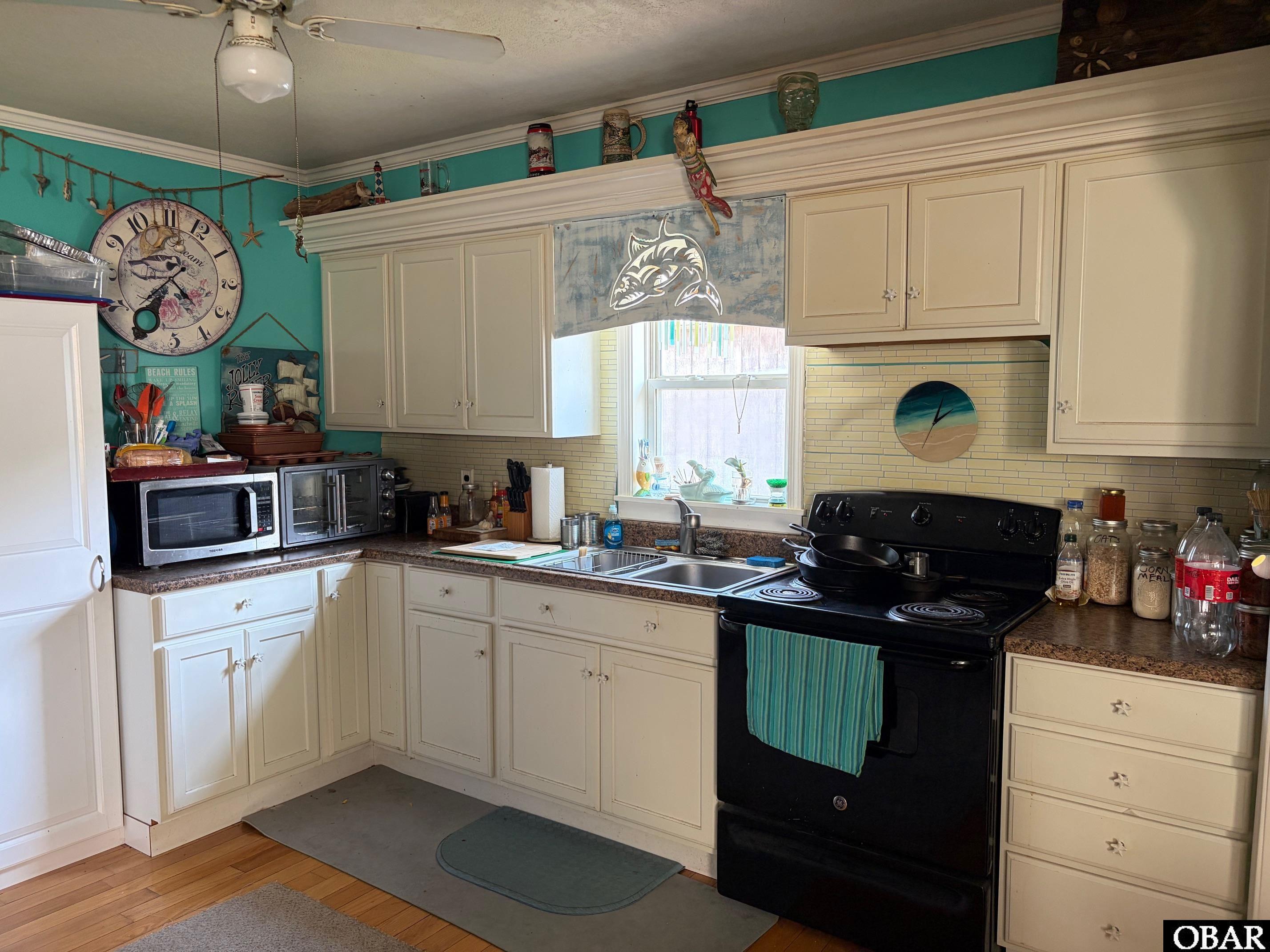Kitchen with cream cabinets, teal walls, and a black range beside a sink under the window.