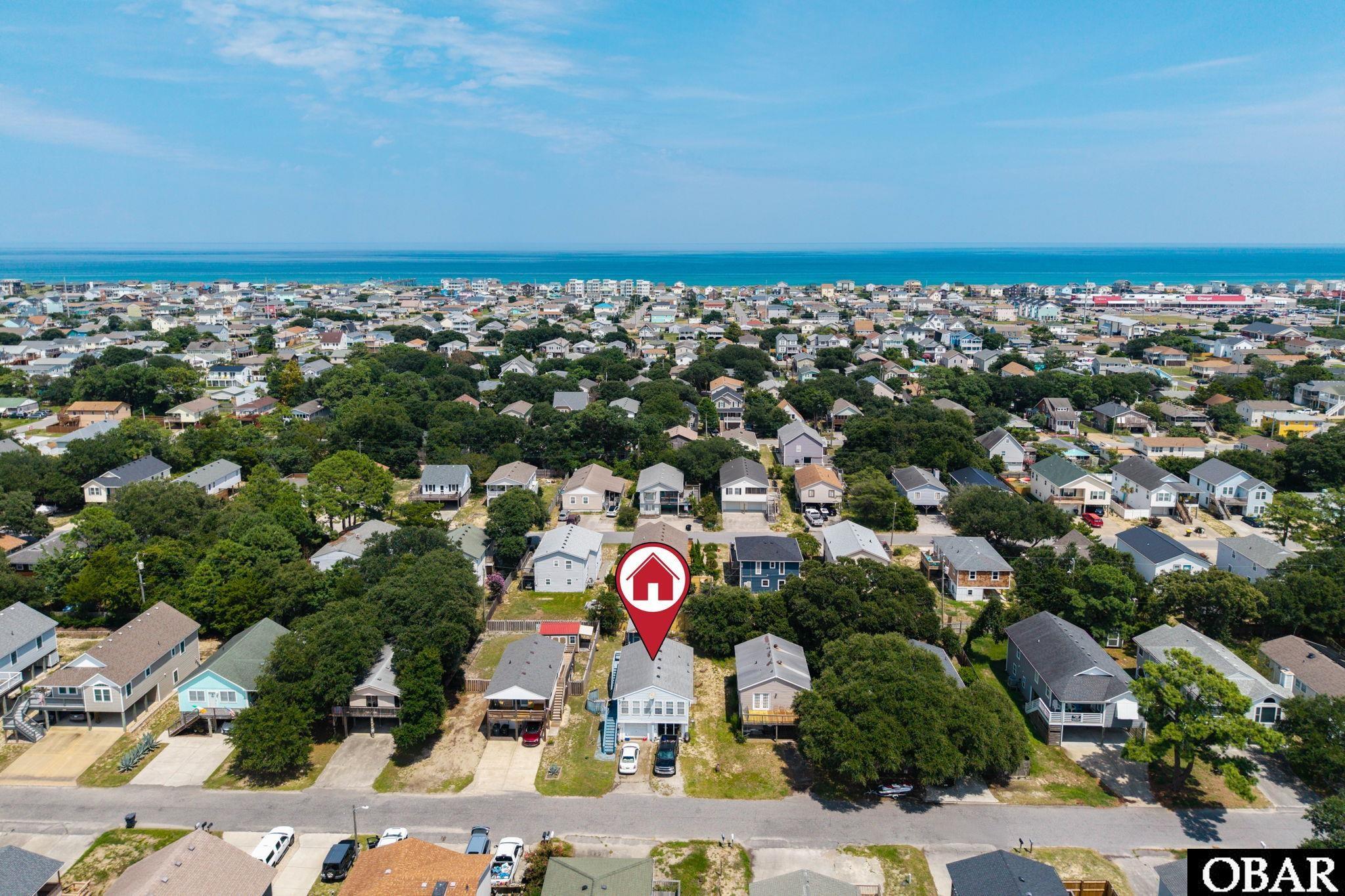 Aerial view of the marked coastal home, with neighborhood houses and ocean on the horizon.