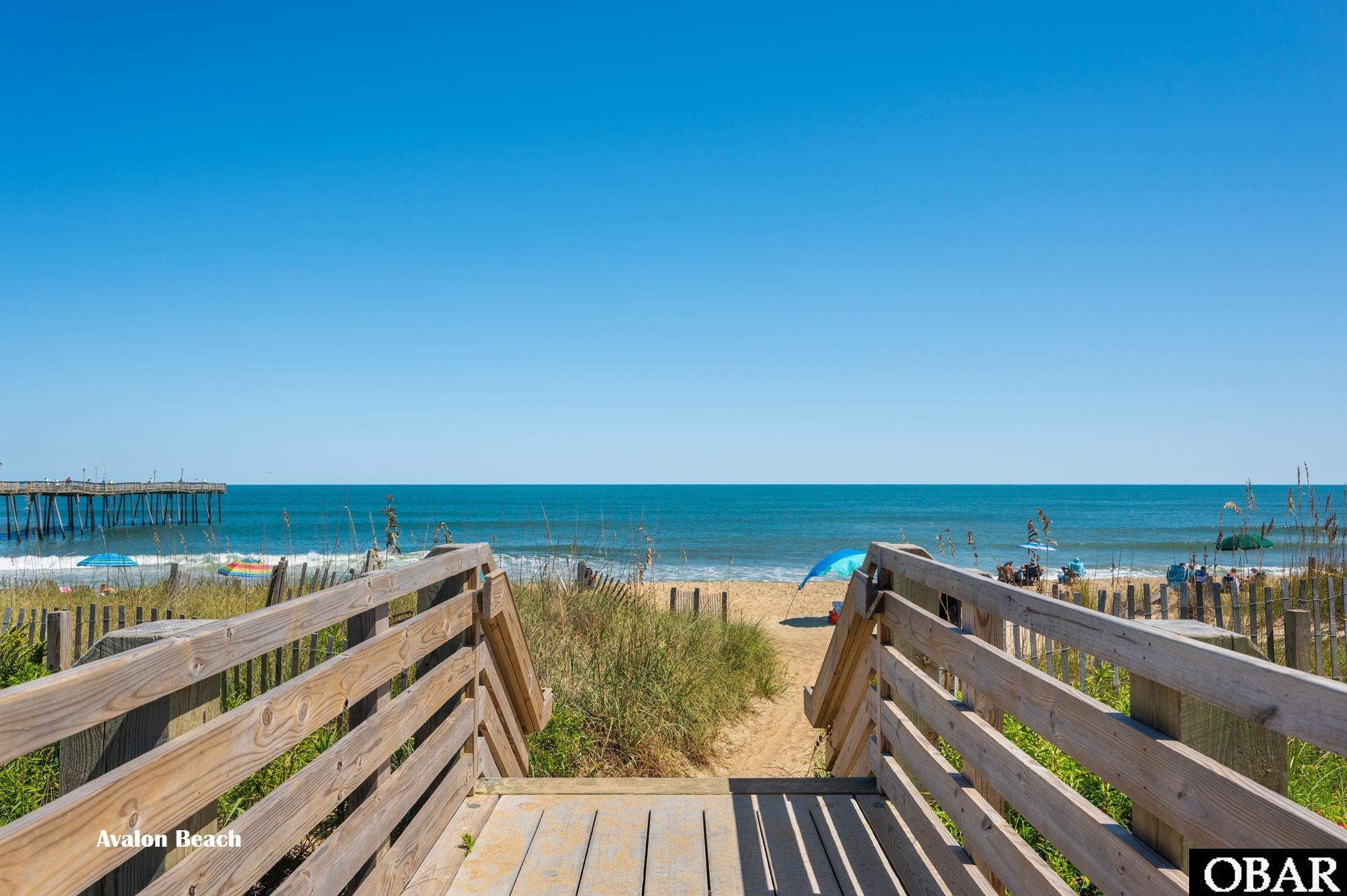 Wooden beach boardwalk leads across grassy dunes to the ocean beside a fishing pier.