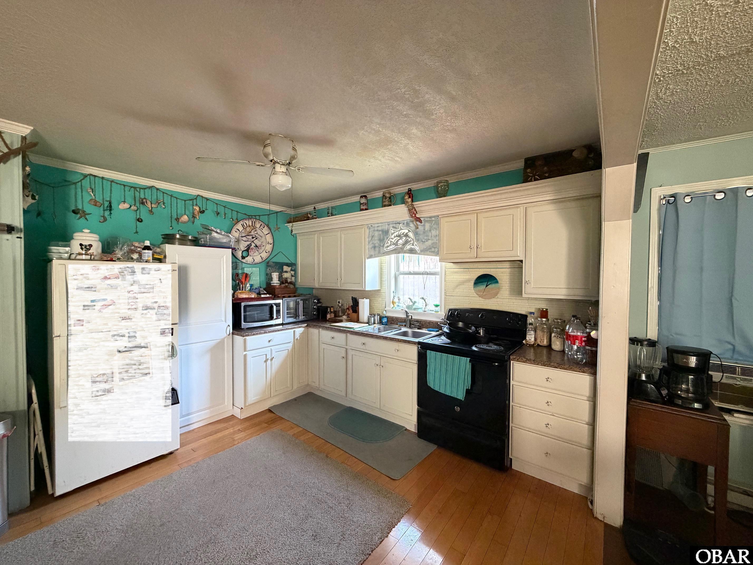 Kitchen with cream cabinets, teal walls, wood floors, and a black range.