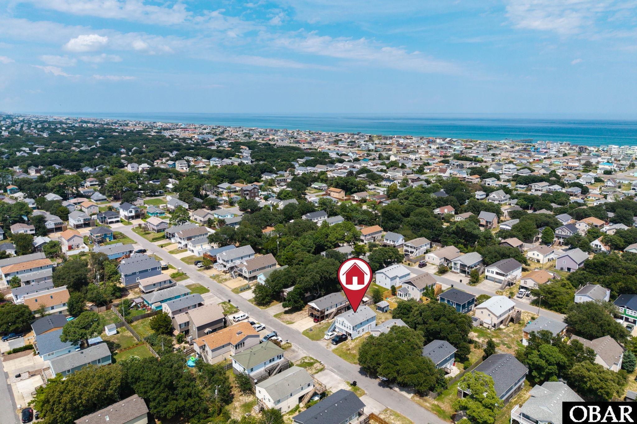 Aerial coastal neighborhood with a red marker identifying a house and the ocean in the distance.