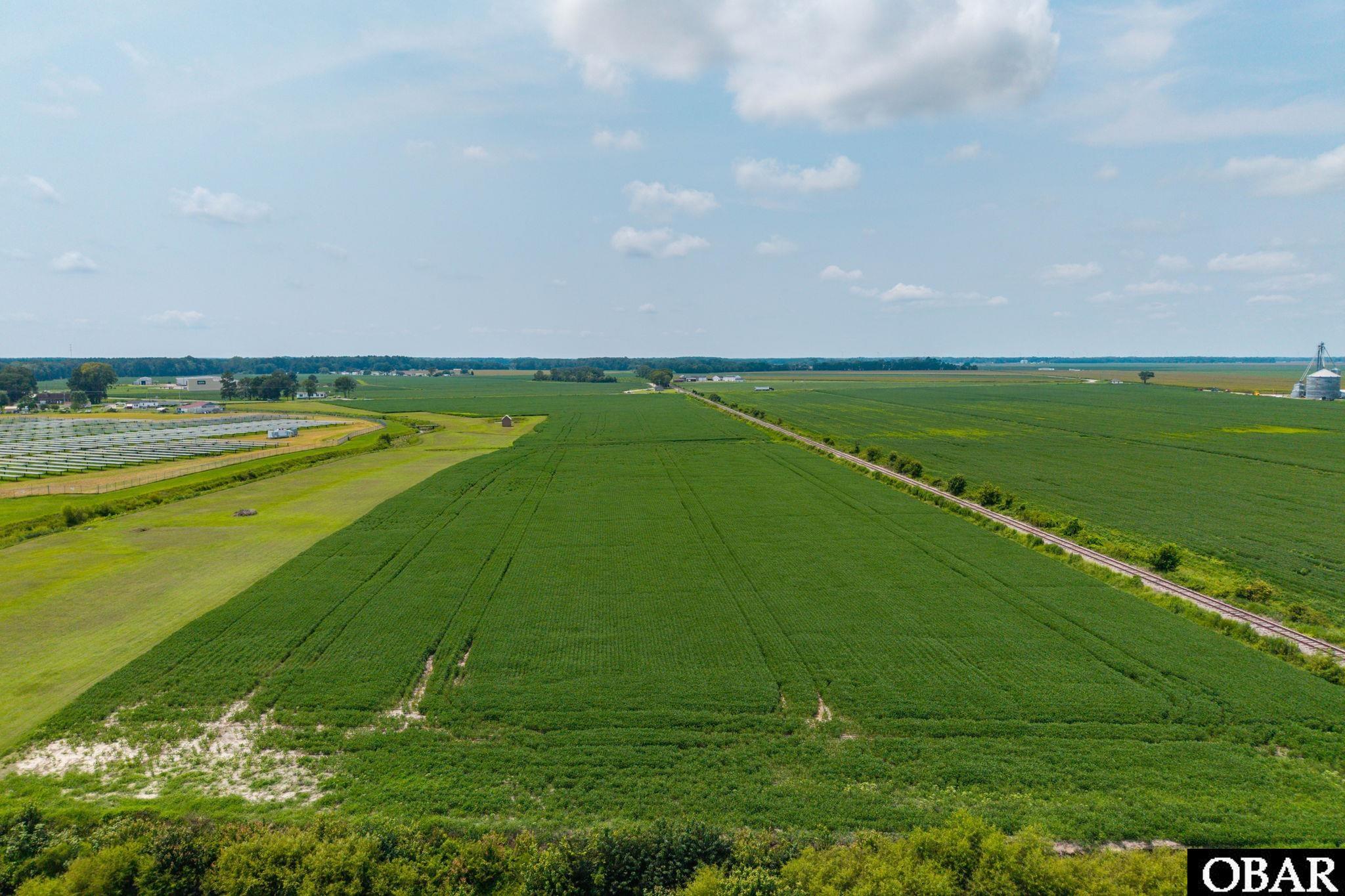 Aerial farmland with a railway track cutting diagonally between green fields and a solar panel array.