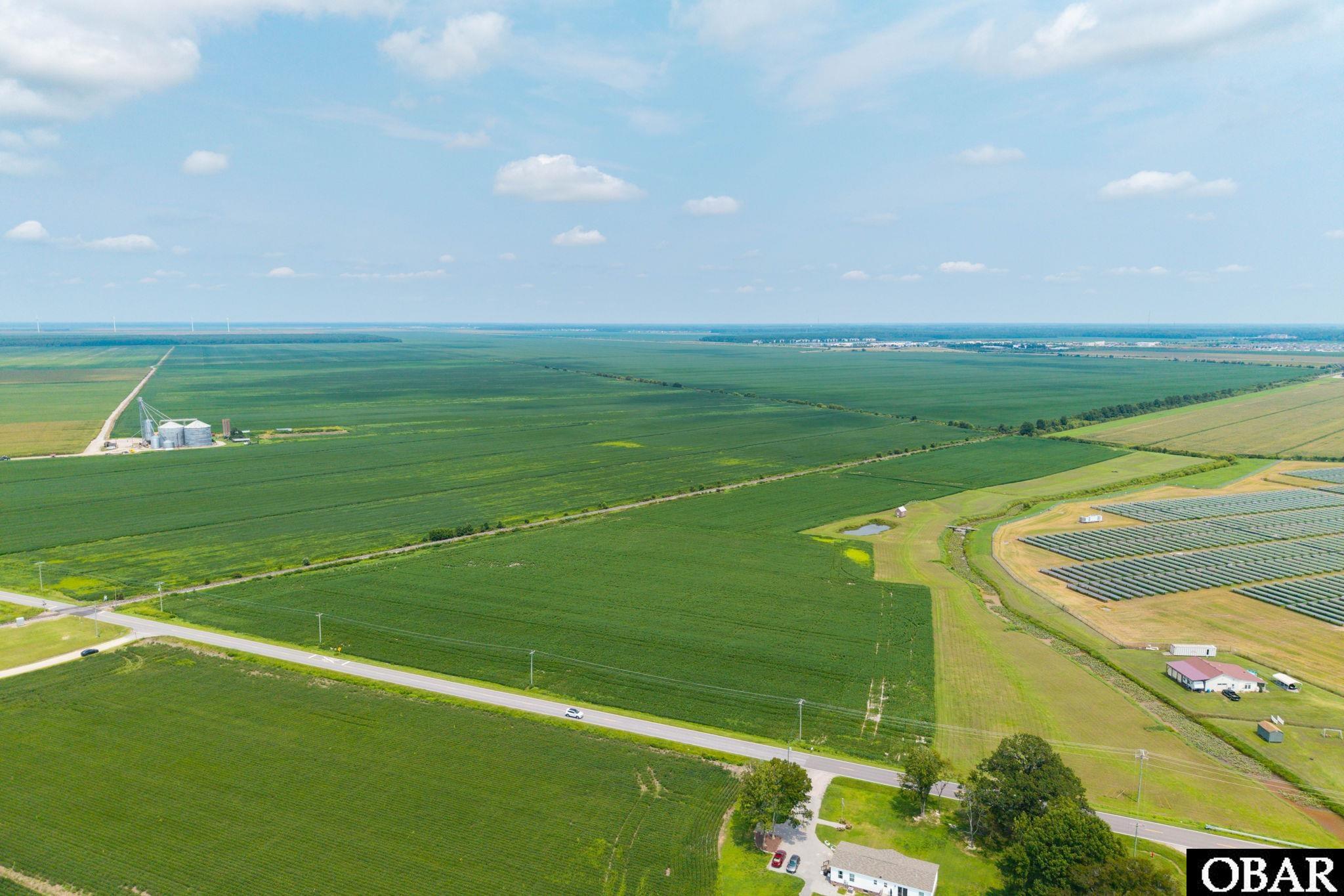 Aerial view of expansive farmland beside a solar array, with grain silos and a road.