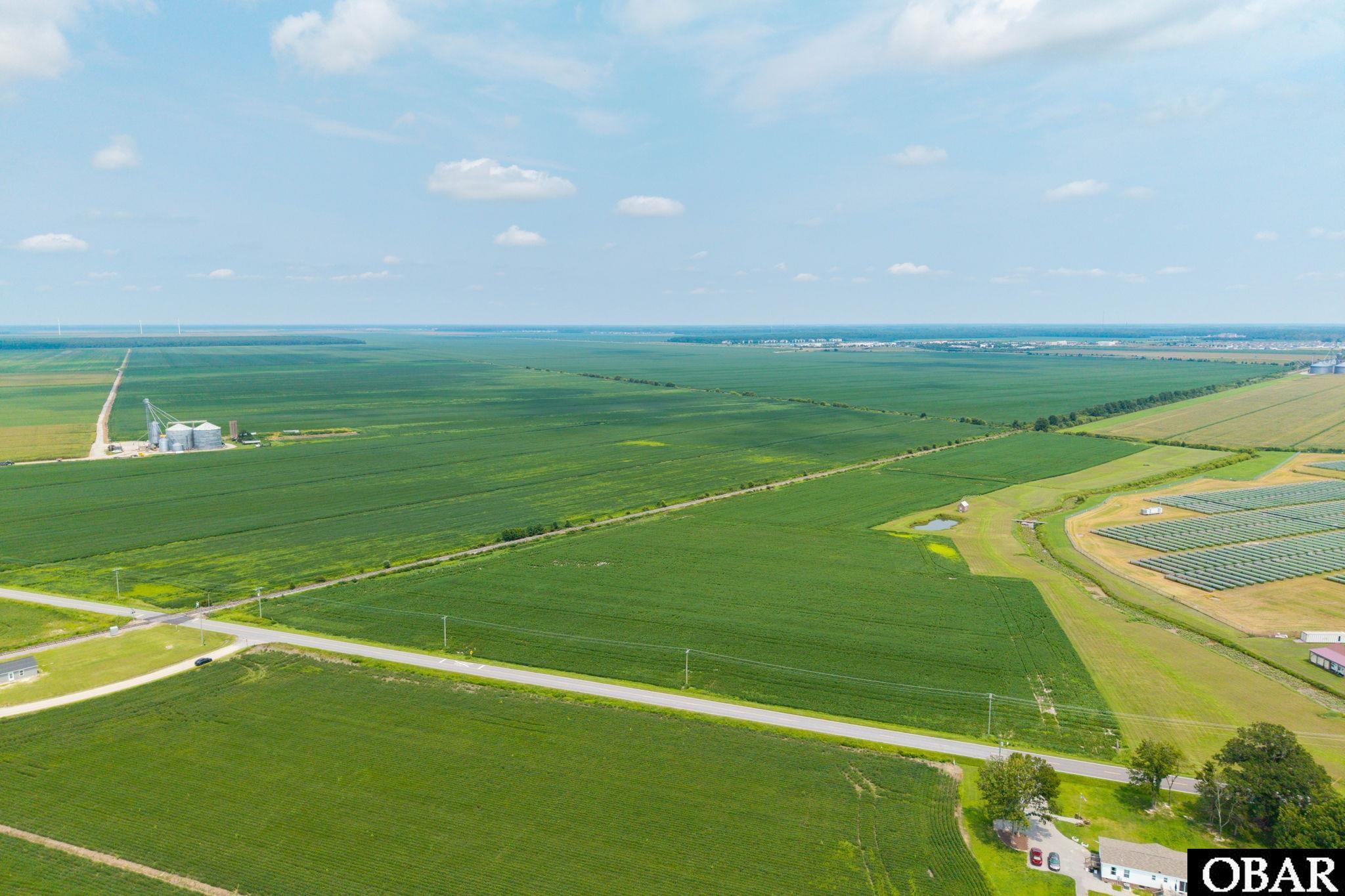Aerial view of expansive farmland divided by a road, with grain silos and a solar array.