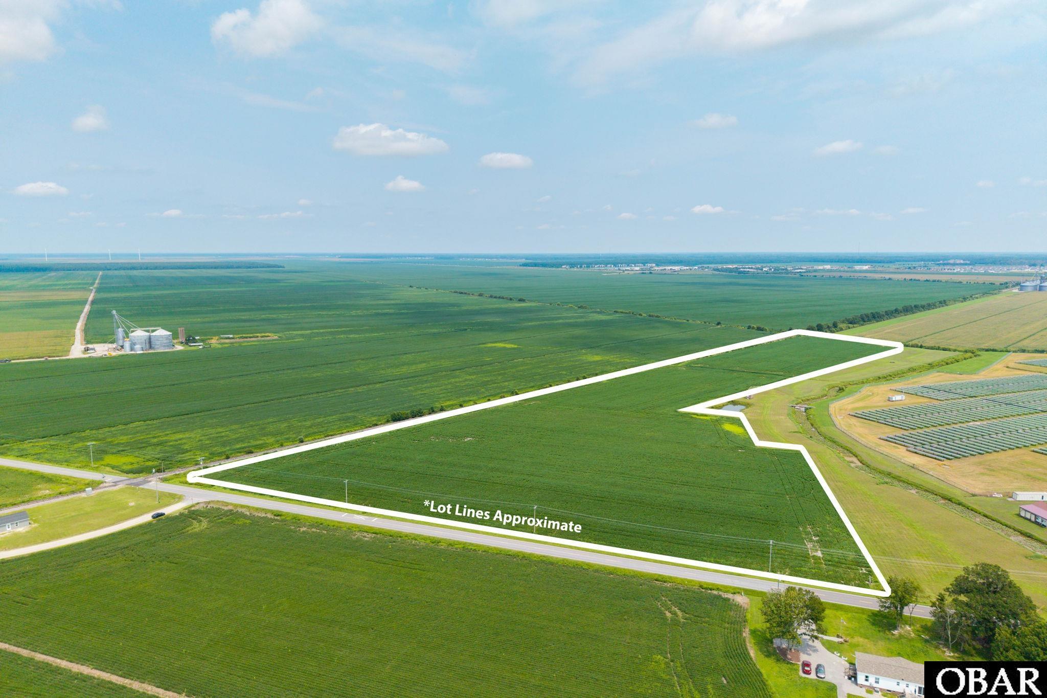 Aerial view of a vacant field parcel outlined in white, with road frontage and neighboring solar panels.