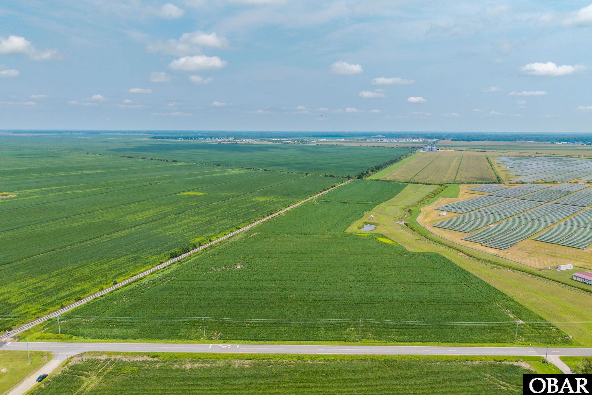 Aerial view of expansive farmland beside solar panel arrays and a road.
