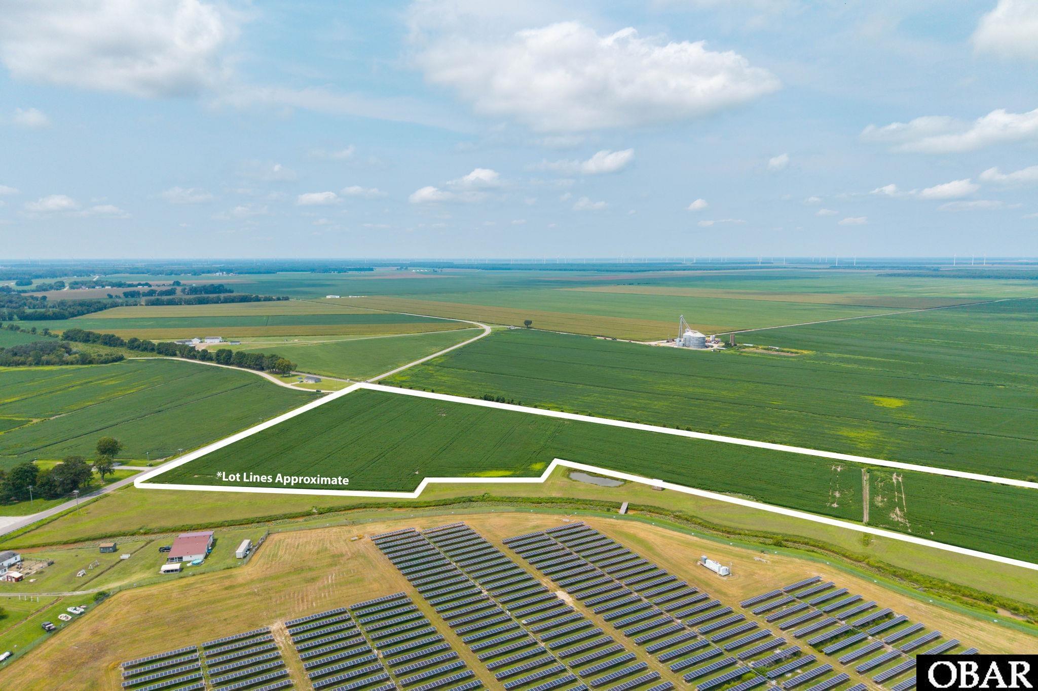 Aerial view of outlined farmland, with solar panels in the foreground and wind turbines on the horizon.