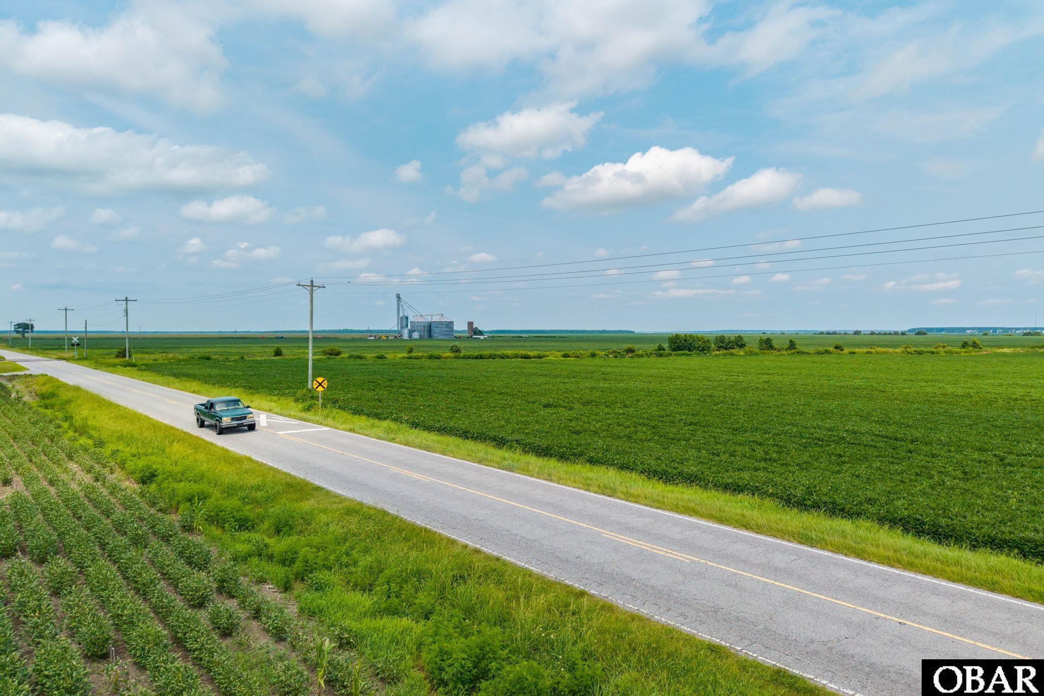 Rural farmland beside a two-lane road, with utility lines and distant grain silos.