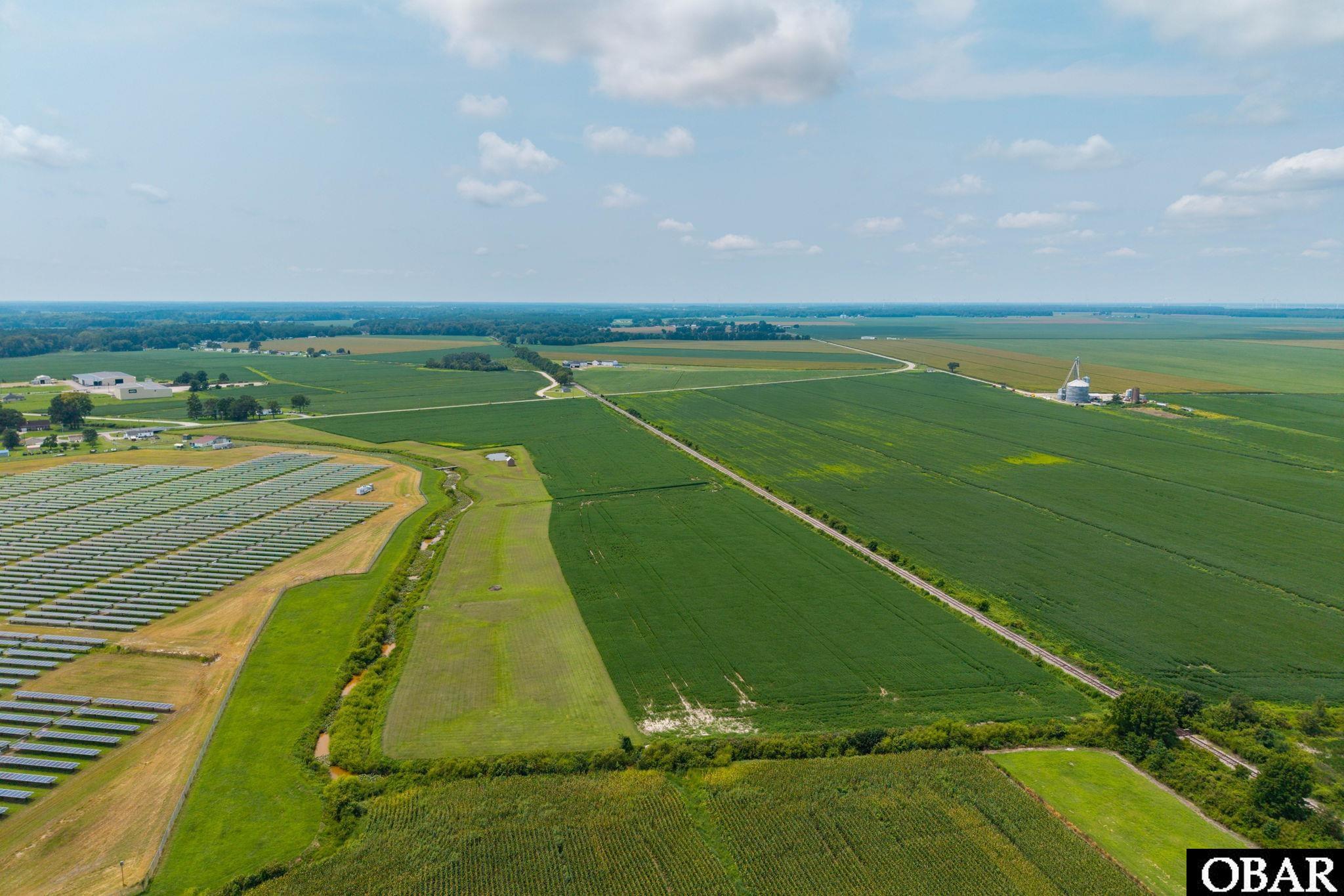 Aerial farmland with expansive green fields, a solar panel array, and distant grain silos.