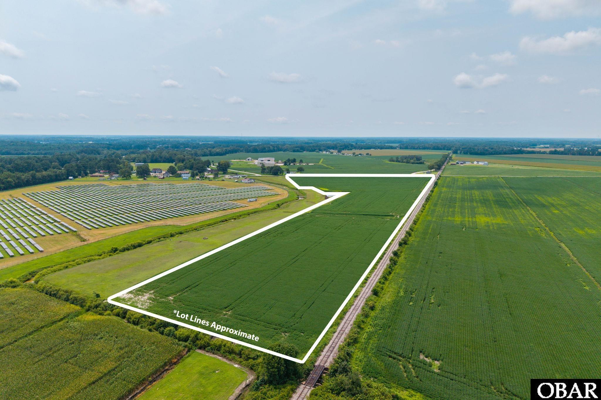 Aerial view of cultivated land outlined beside a solar panel array and railroad tracks.